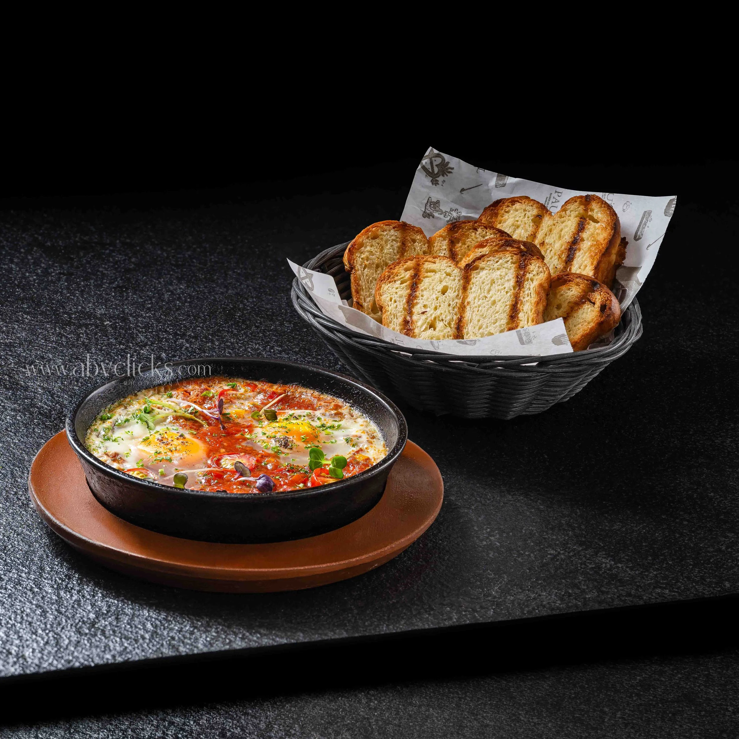 Slices of grilled bread in a basket with parchment paper, placed on a dark textured surface.