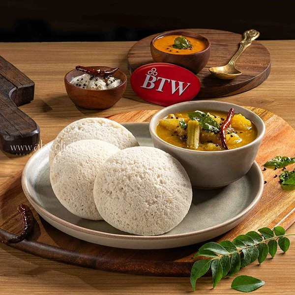 Indian meal with three idlis on a plate, served with sambar and chutney, accompanied by a small bowl of orange curry.