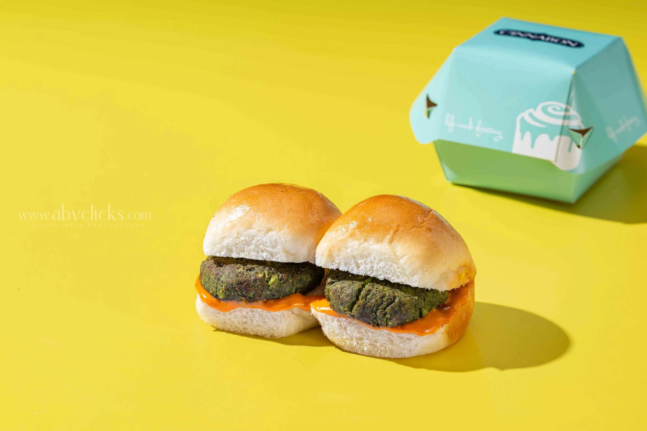 Close-up of two sliders with veggie patties, with a blue and green box in the background on a yellow surface.