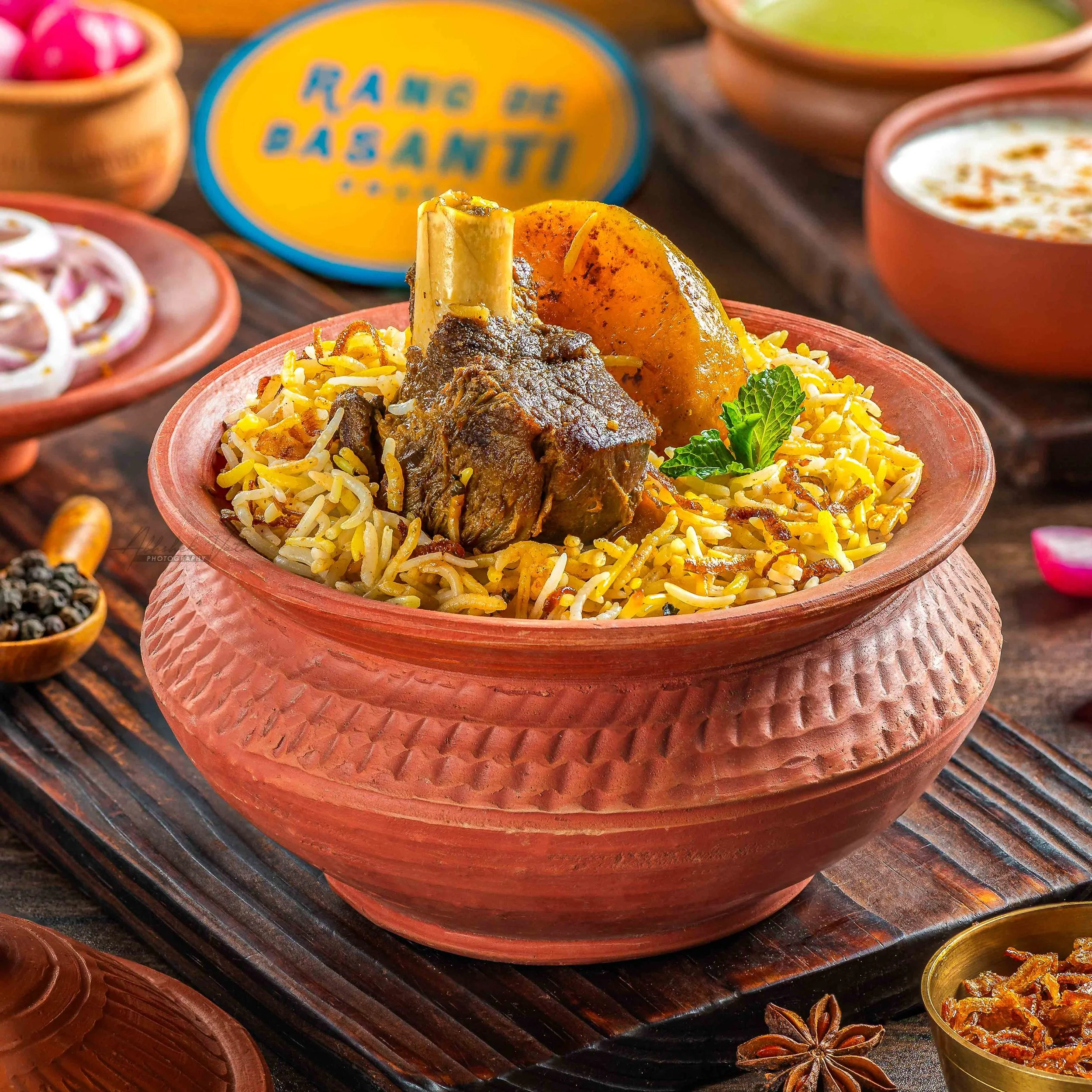 A traditional Indian dish called Biryani served in a terracotta bowl, garnished with fresh green herbs and accompanied by side dishes and spices on a wooden surface.