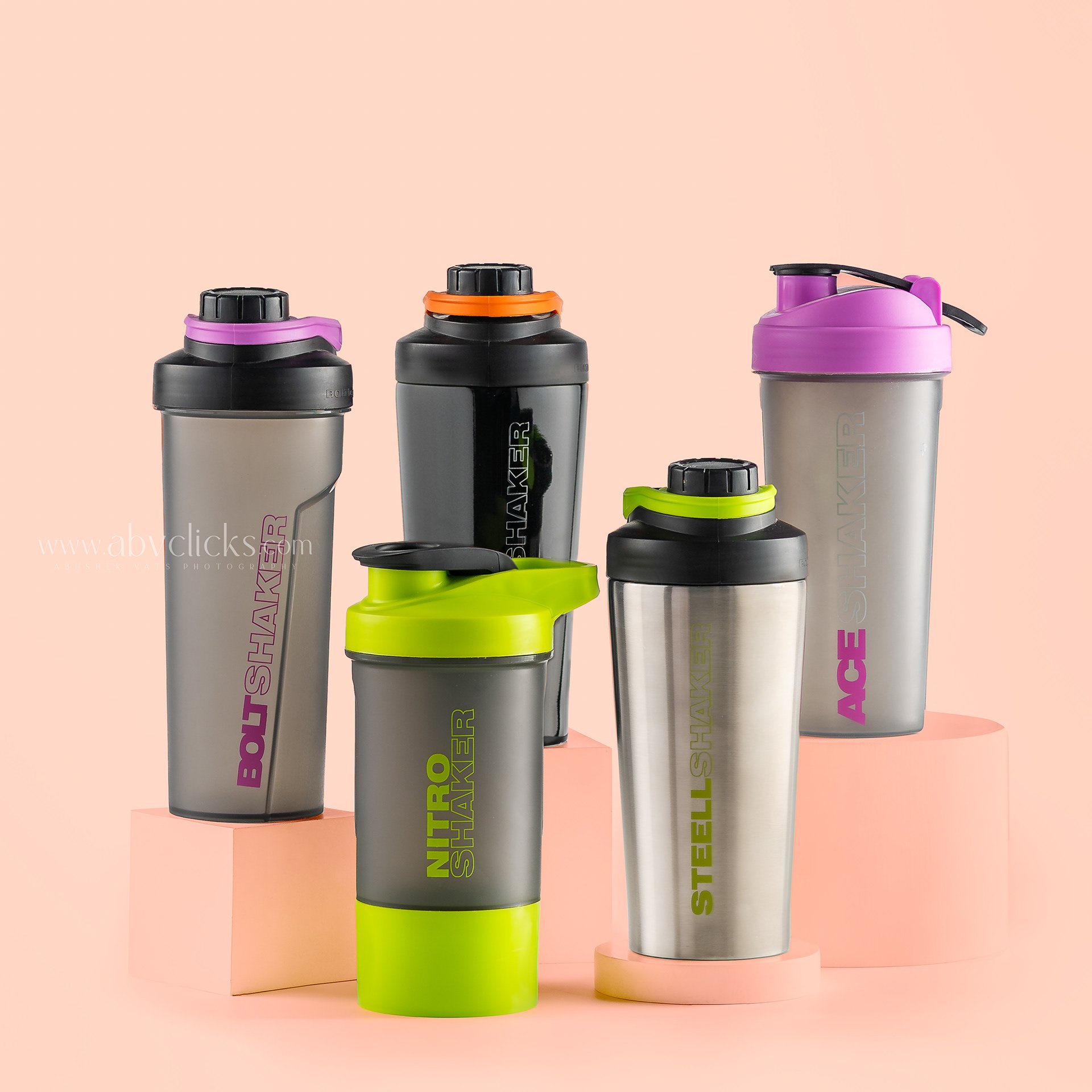 Set of colorful shaker bottles with different caps, including purple, orange, pink, and green, standing on a pastel background.