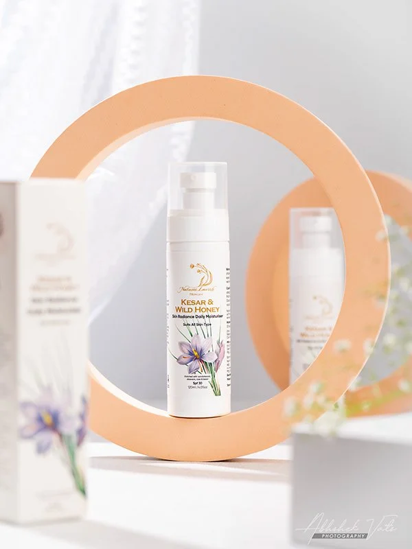A skincare product labeled 'Kesar & Wild Honey' with a floral illustration, placed in front of a round mirror in a bright, minimalist setting.