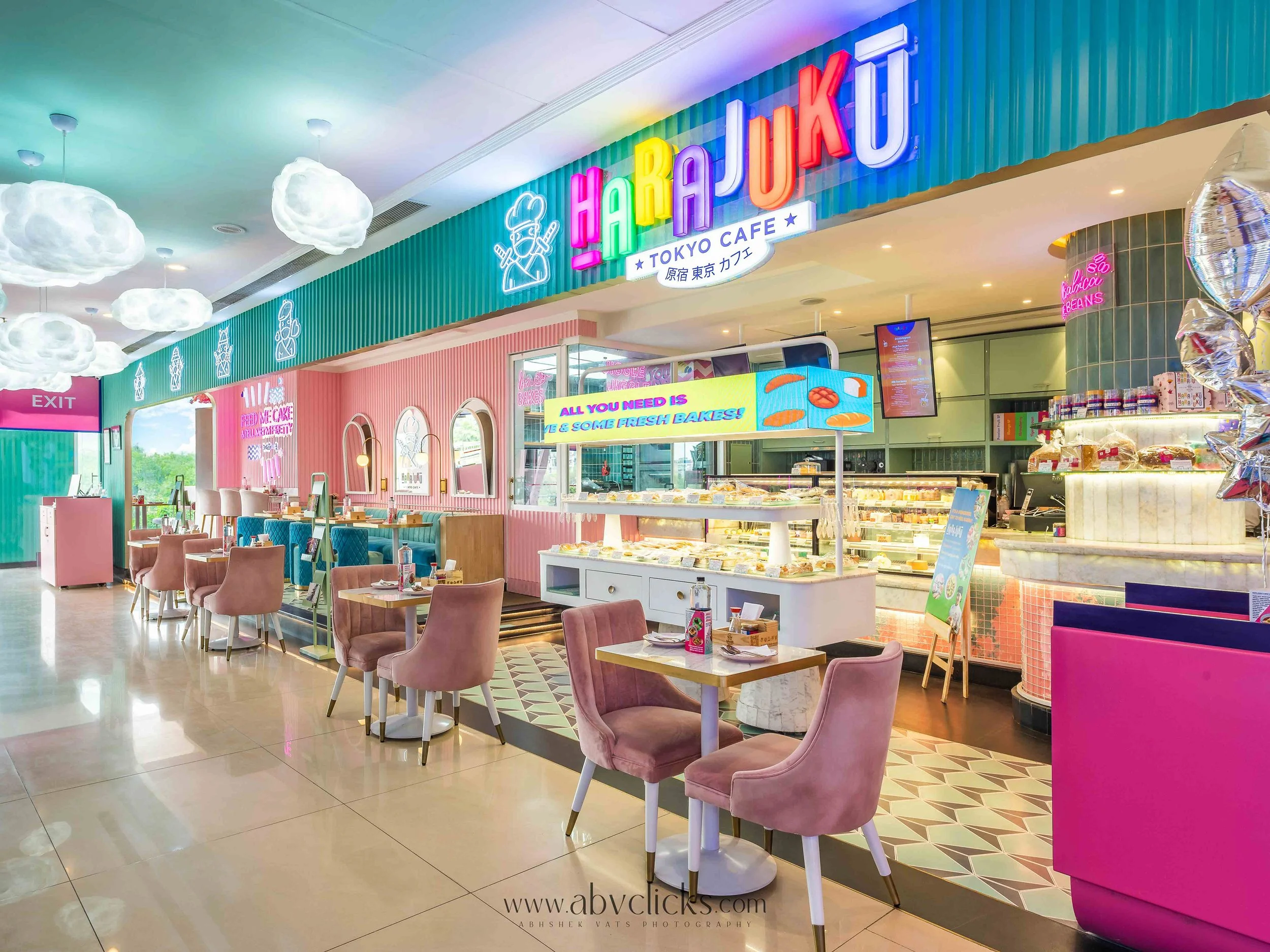 Interior of a colorful cafe called Harejuku, with pastel pink, green, and blue decor, cloud-shaped ceiling lights, pink chairs, and baked goods display case.