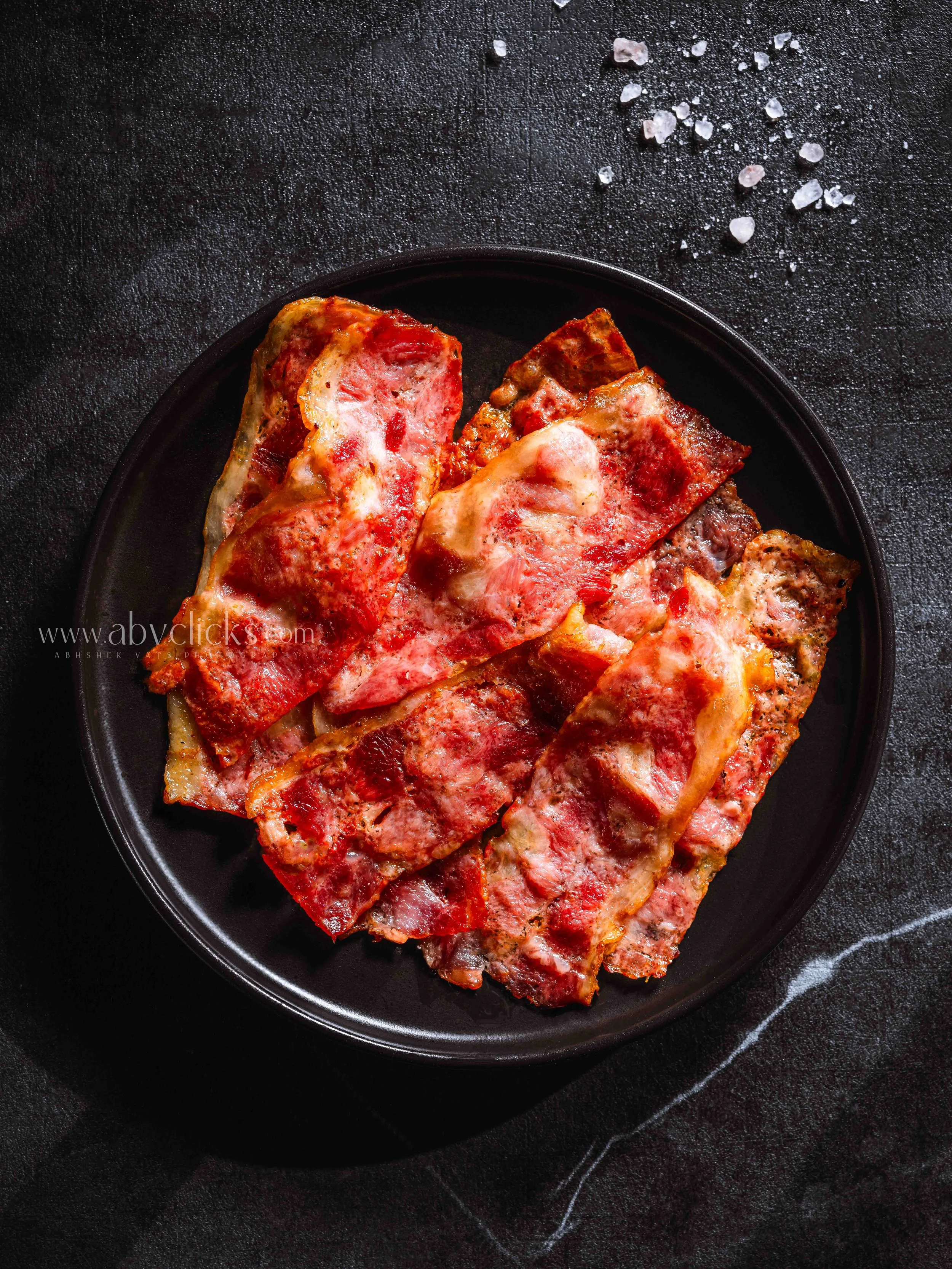 Close-up of cooked pizza slices on a black plate, placed on a dark textured surface, with coarse salt scattered nearby.