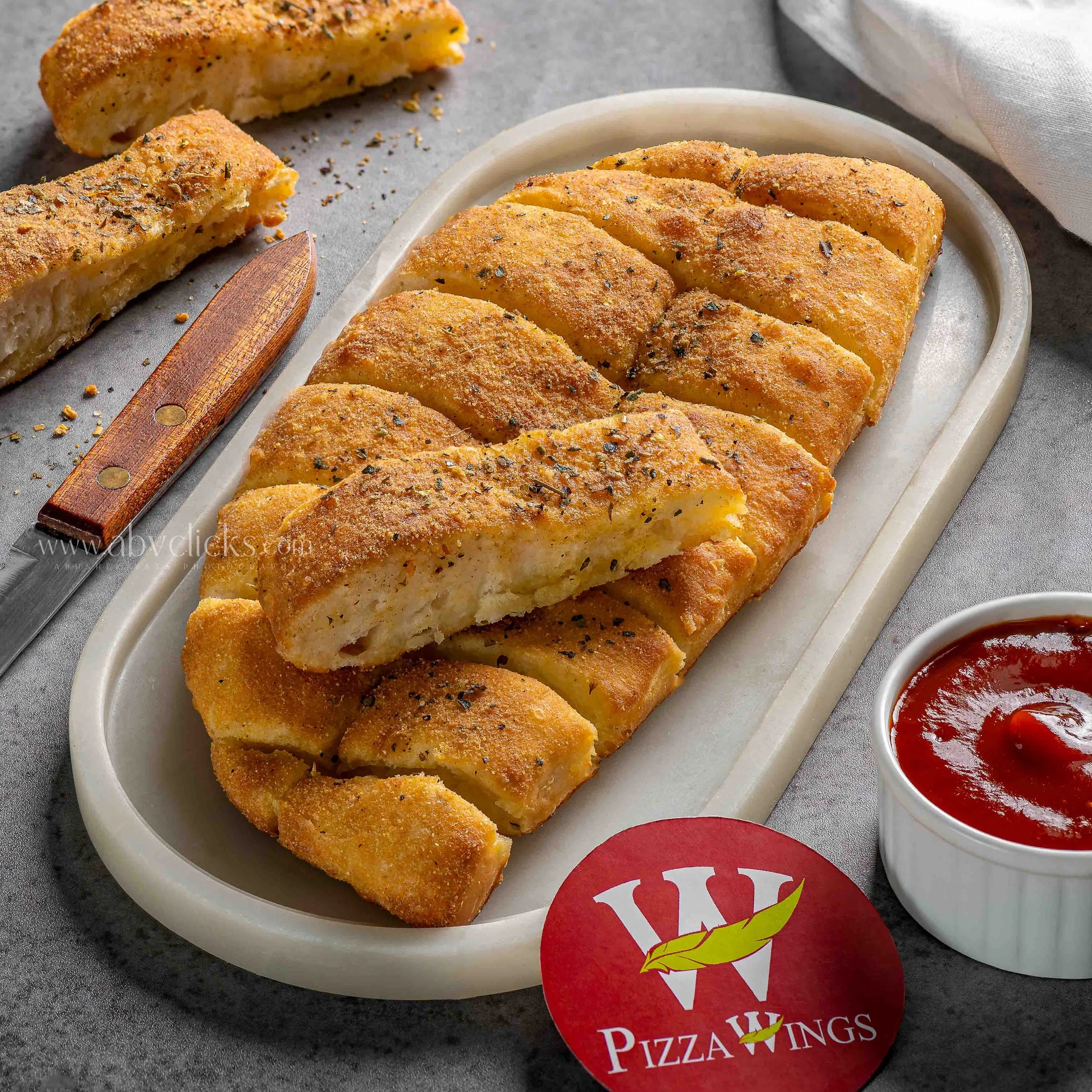Slices of garlic Parmesan bread on a white plate with a small bowl of marinara sauce, set on a grey surface.