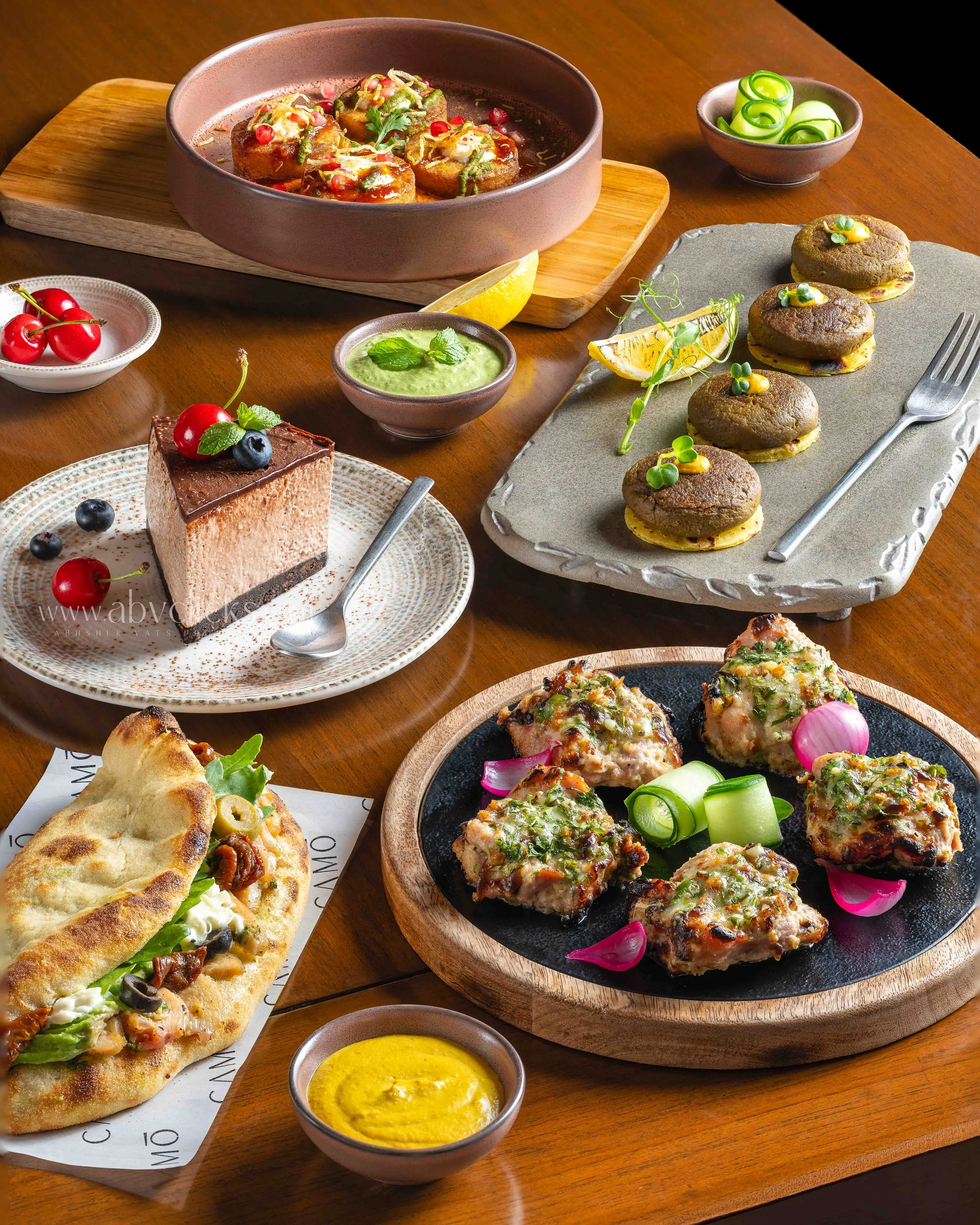 Assorted Indian cuisine including kebabs, naan bread, rice, dips, and chutneys on a wooden table.