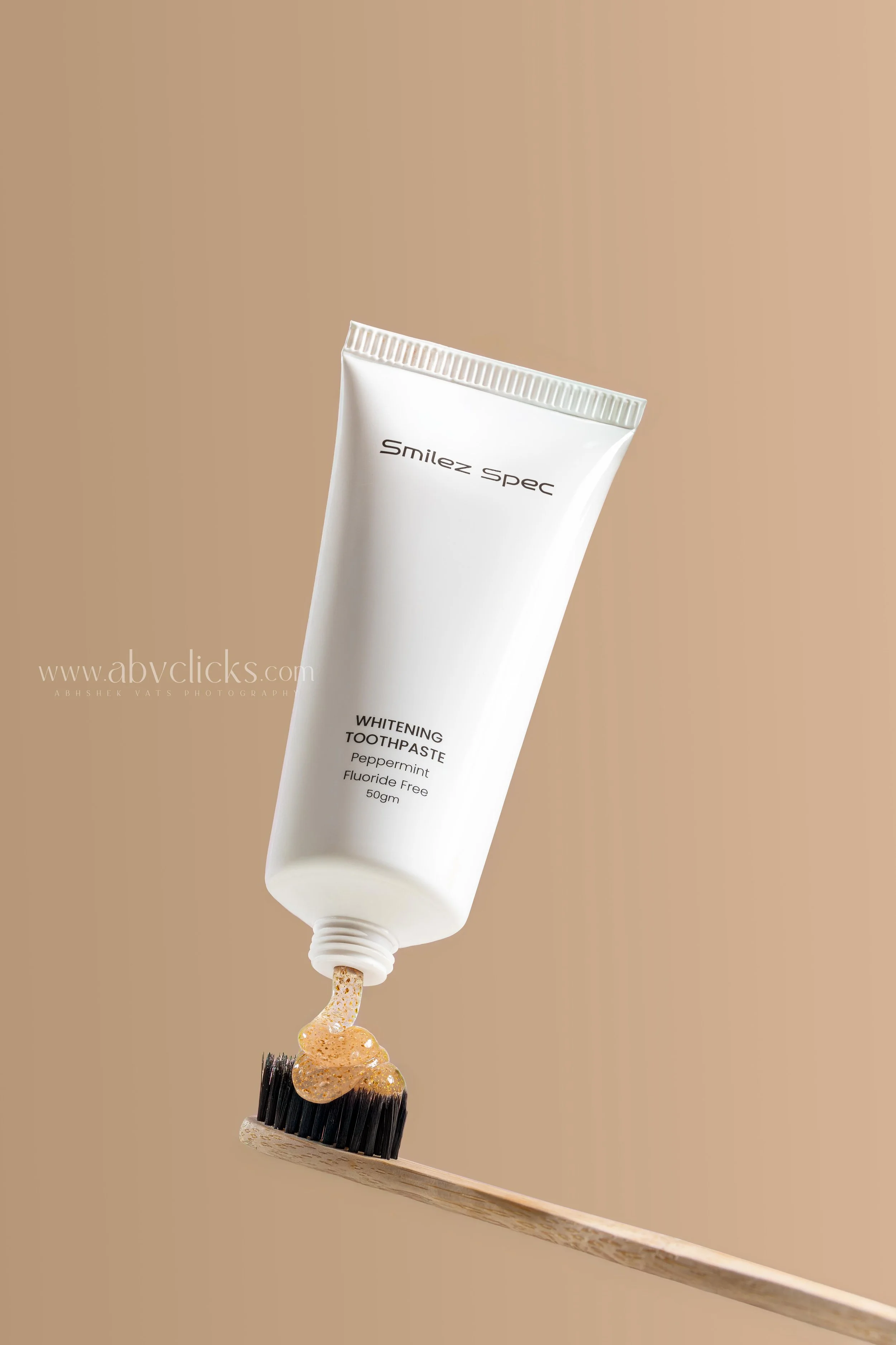A tube of whitening toothpaste labeled 'Smilez Spec,' peppermint flavor, fluoride free, 50g, shown releasing a dab onto a toothbrush.