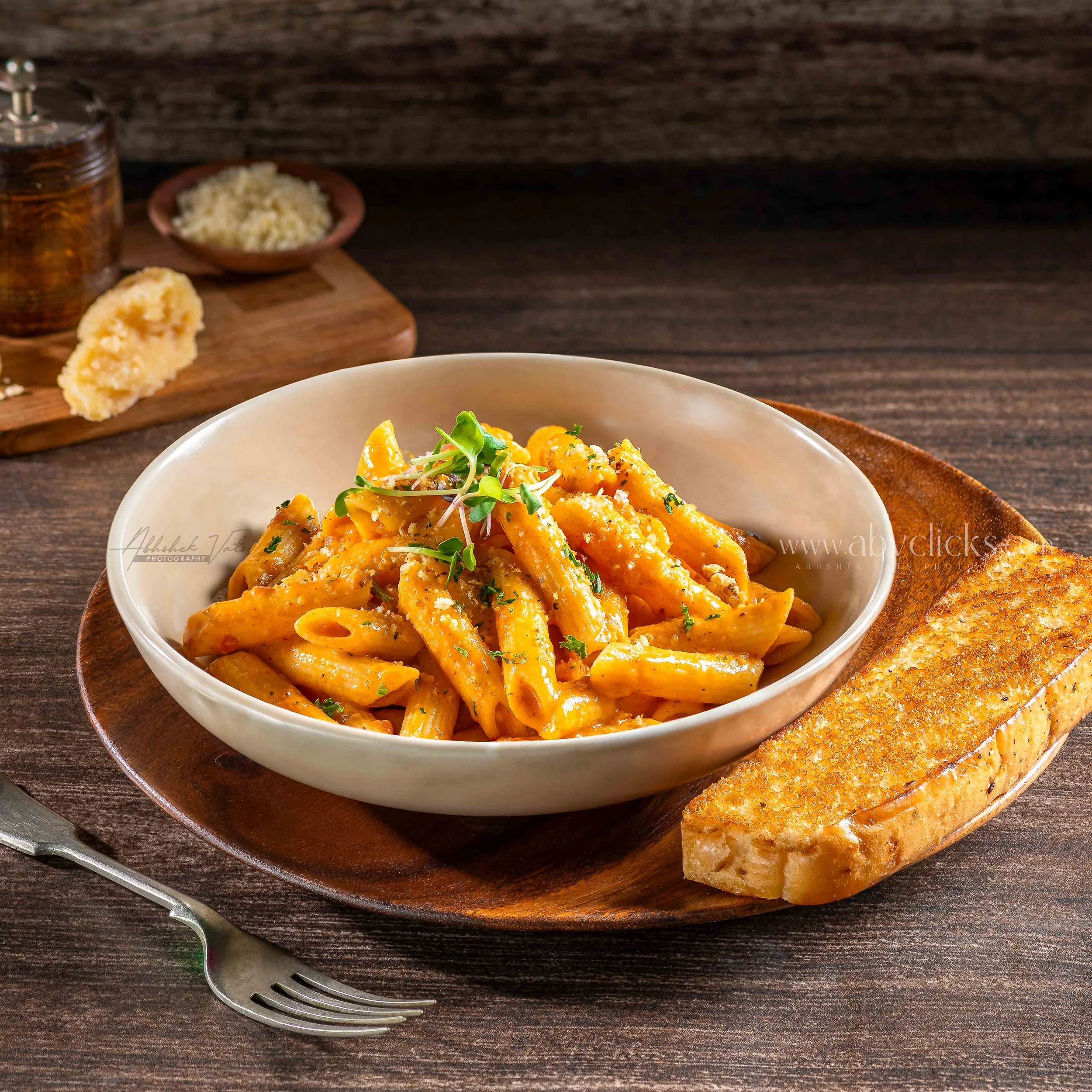 Bowl of creamy pasta with herbs, served on a wooden table with grated cheese and bread in the background.