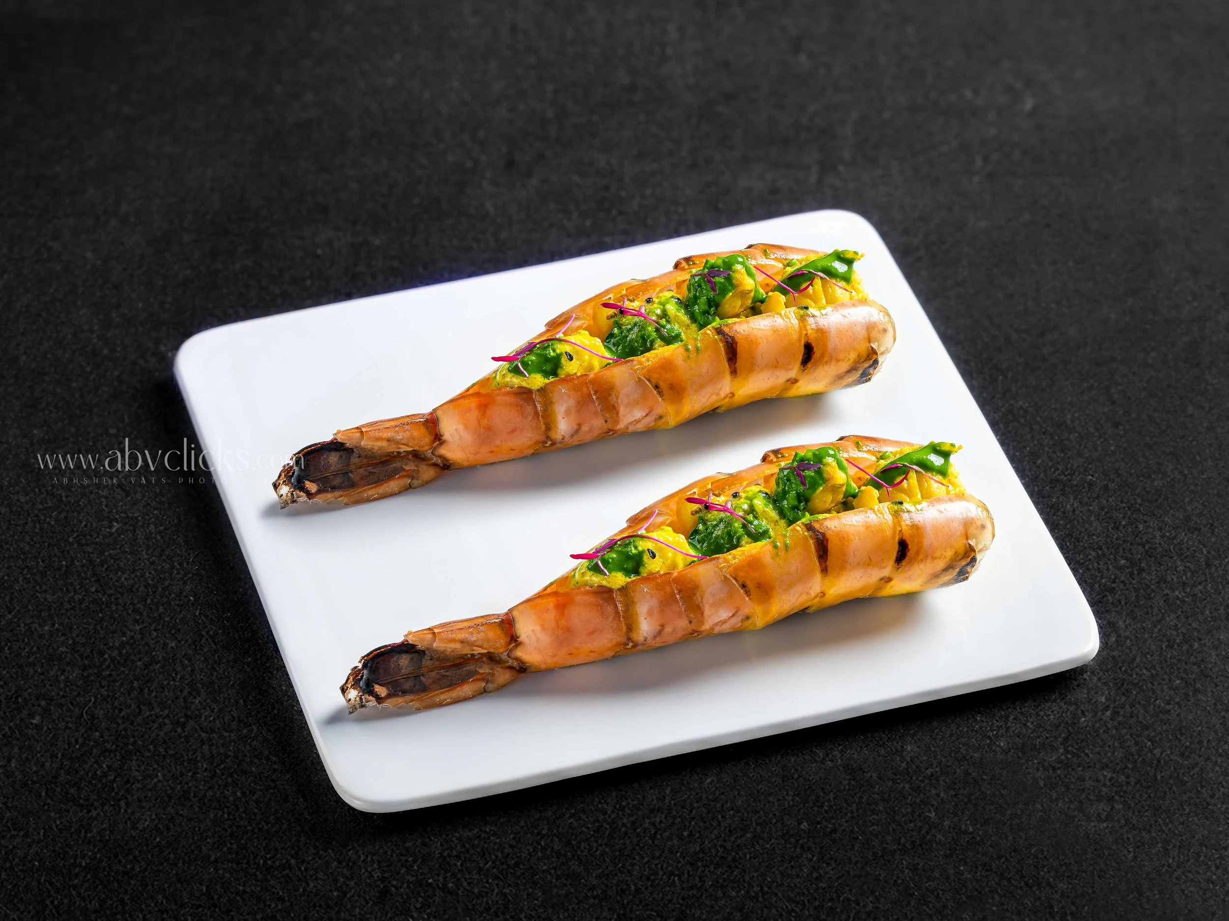 Three grilled shrimp with stuffed filling on a white rectangular plate against a black background.