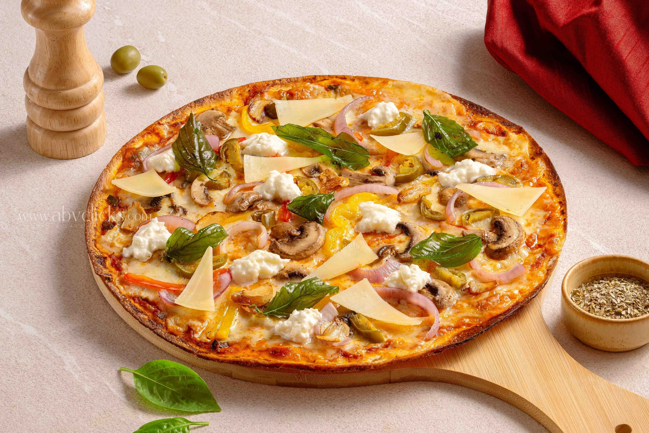 A pizza with cheese, mushrooms, bell peppers, onions, and fresh basil leaves on top