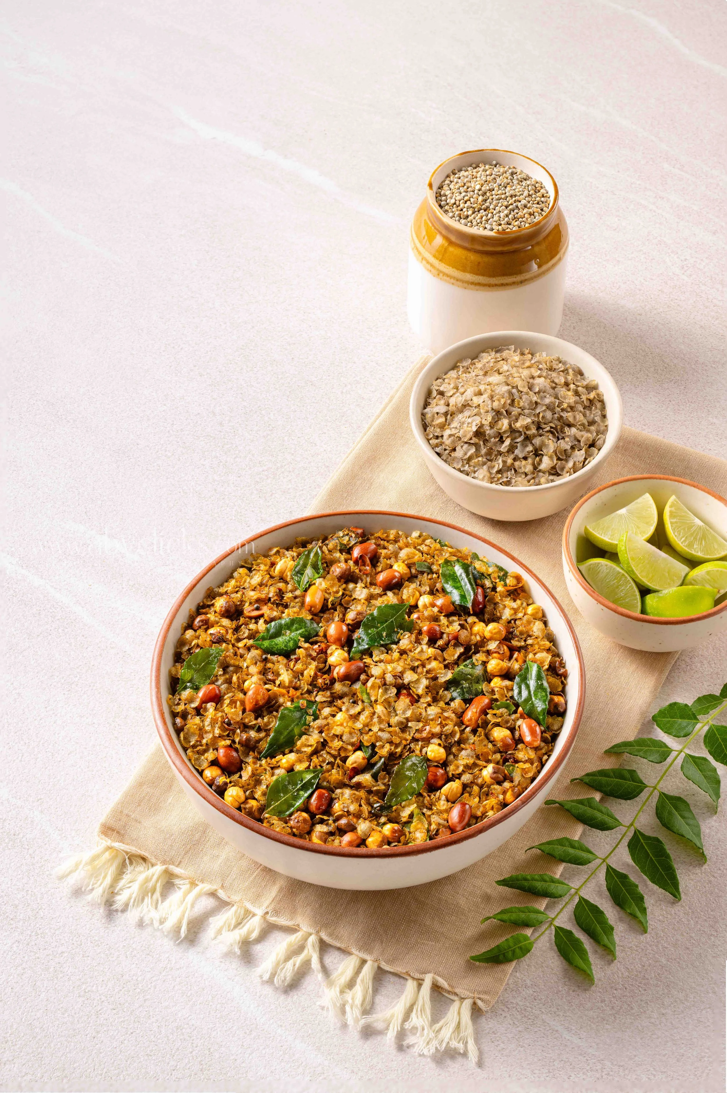 A bowl of cooked lentils garnished with curry leaves, with lime wedges, a bowl of uncooked lentils, and seasonings on a table.