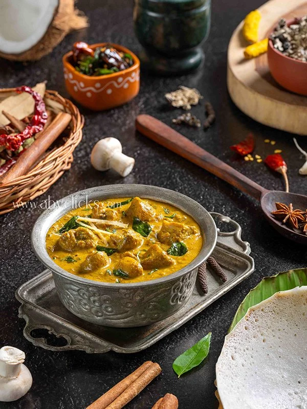 A bowl of Indian chicken curry served on a silver plate with spices and garnishes around it.