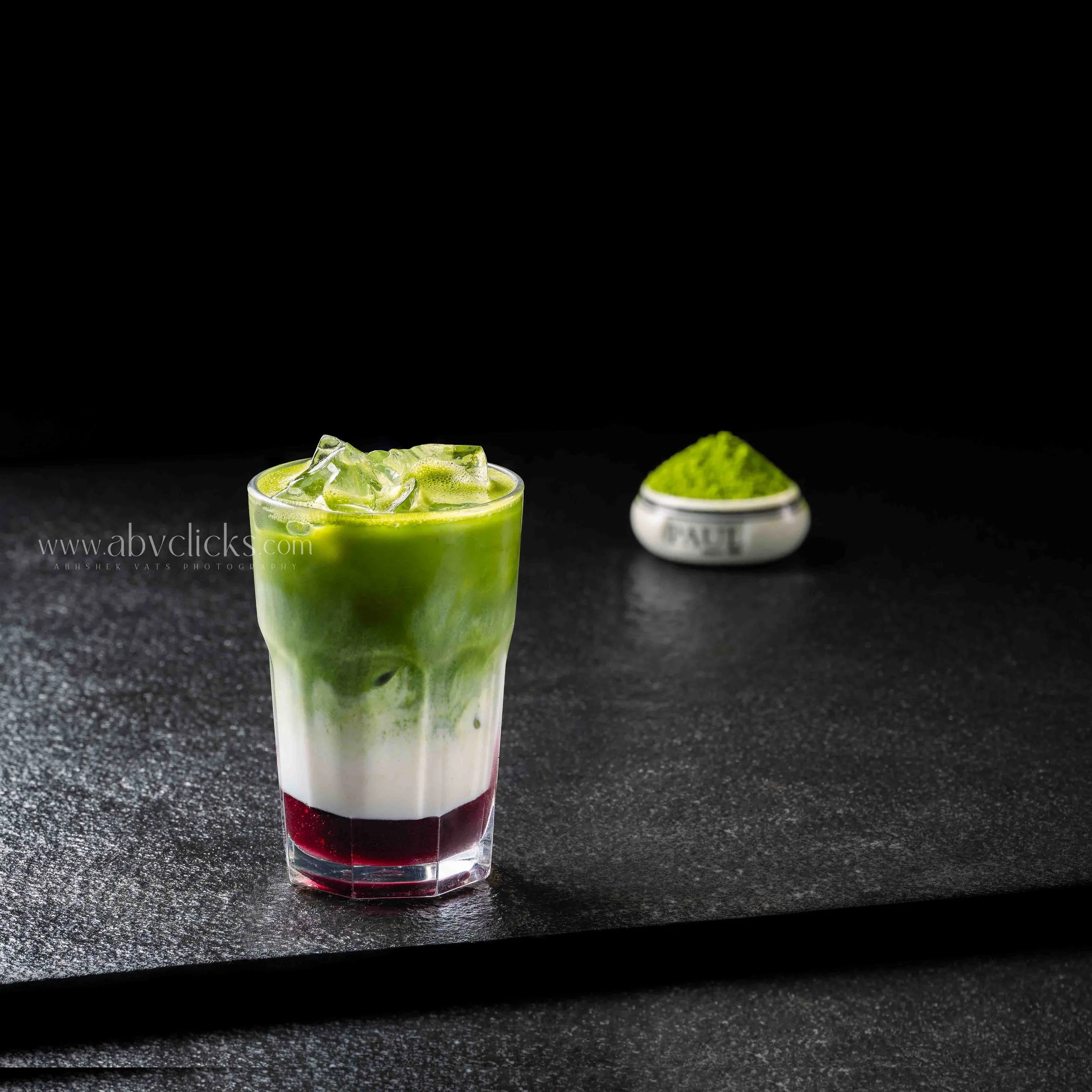 Three colorful layered smoothies in tall glasses on a black surface, with a dark background.