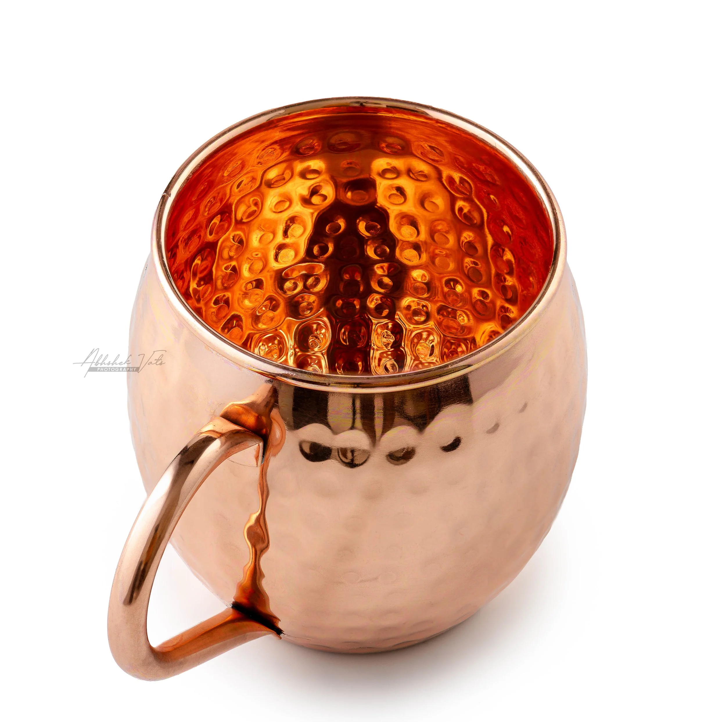 Top view of a copper-colored mug filled with a dark, carbonated beverage, showing bubbles on the surface, with a white background.