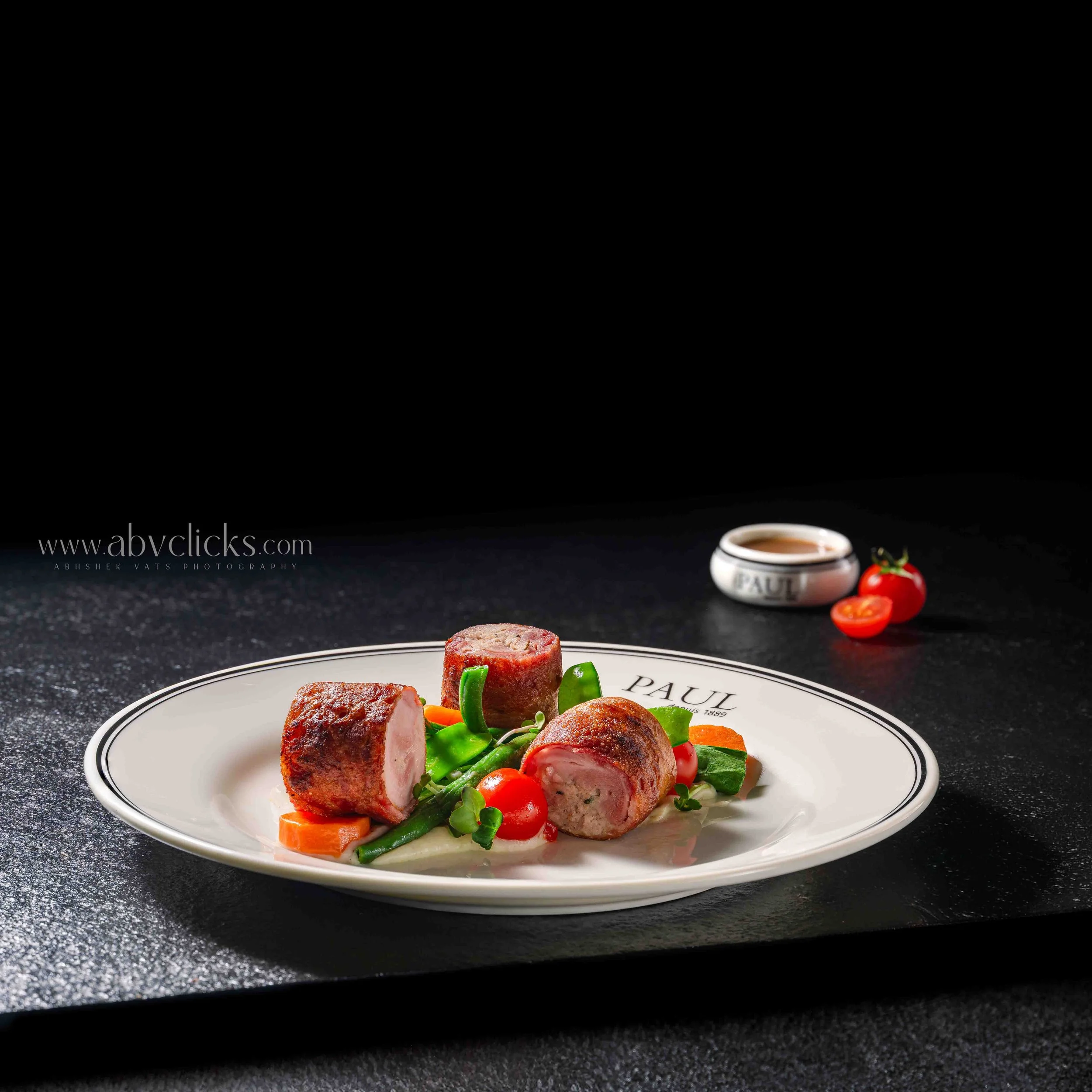 Plate with cooked sausage slices, cherry tomatoes, green beans, and sliced carrots against a black background
