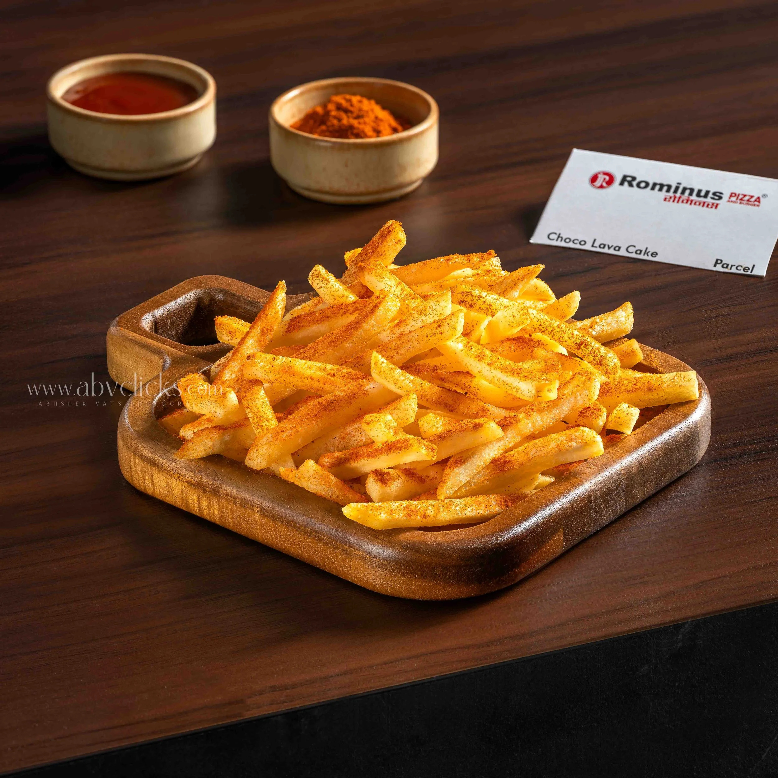 French fries sprinkled with reddish-orange seasoning on a wooden serving tray.