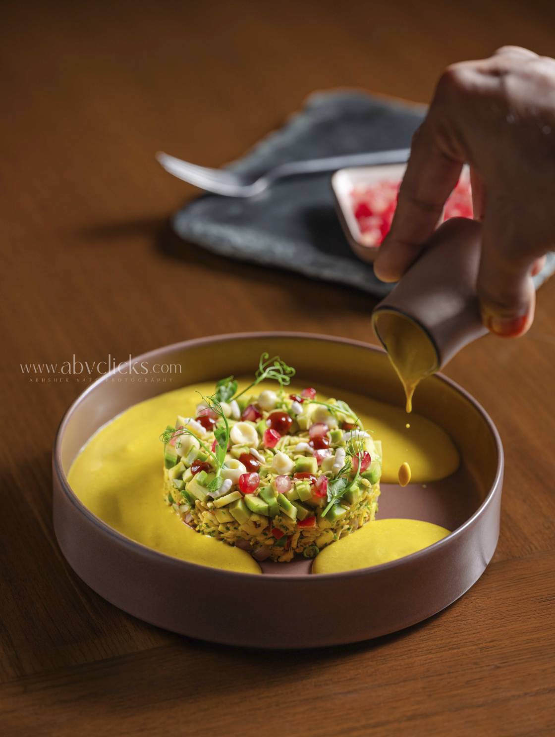 A plated dish with a colorful vegetable and ice cream garnished with microgreens, with a hand pouring sauce or syrup onto it.