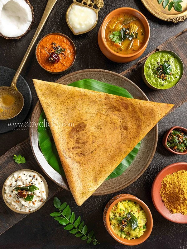 A large Indian naan bread on a plate with various bowls of Indian dishes and condiments around it.