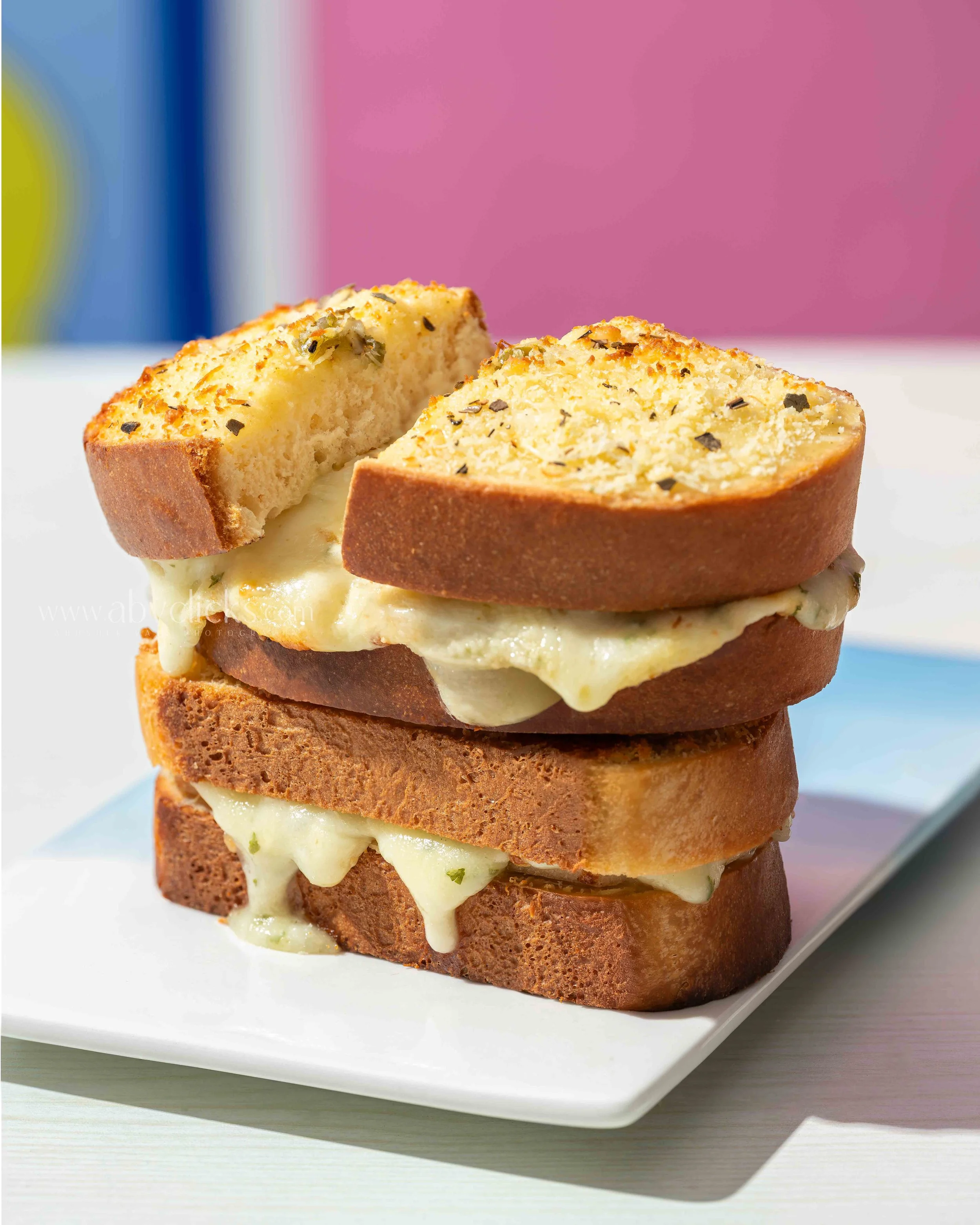 Close-up of a toasted bread slice with melted cheese and herbs on top, stacked on a white plate.