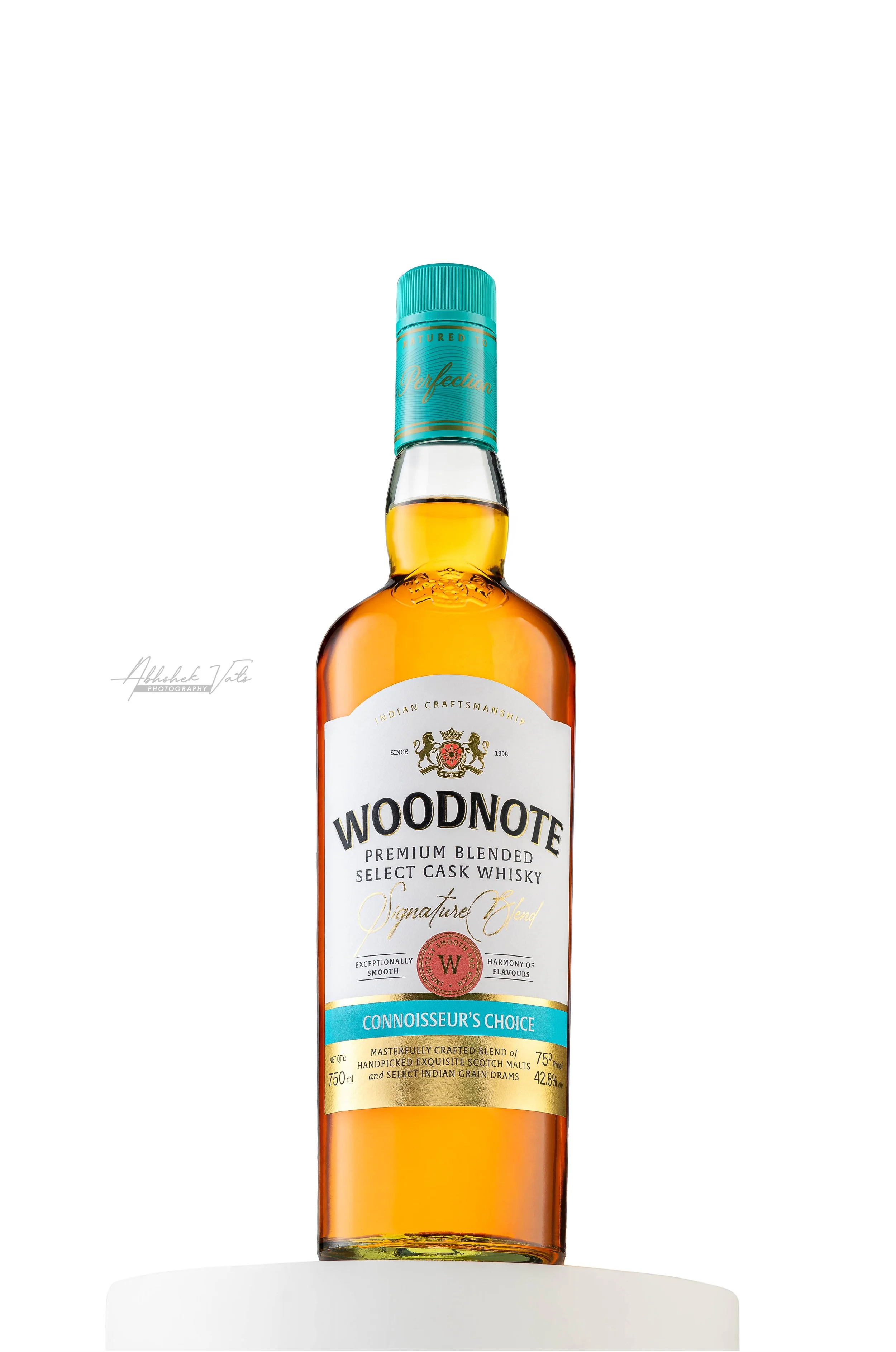 Bottle of Woodnote Premium Blended Select Cask Whisky with a teal cap, white and gold label, and amber liquid visible through the glass
