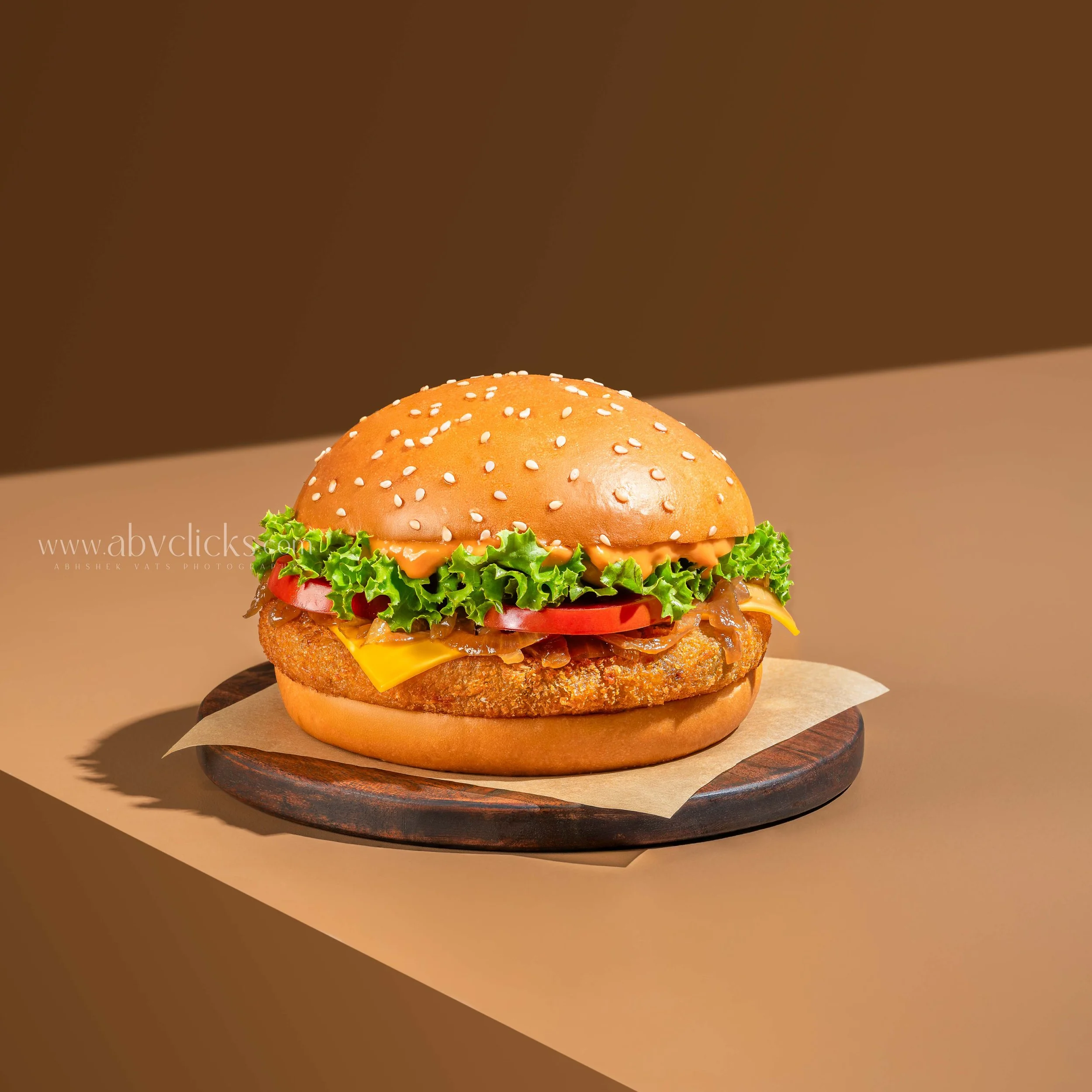 Close-up of a sesame seed hamburger bun on a round wooden plate with a background featuring shades of brown.