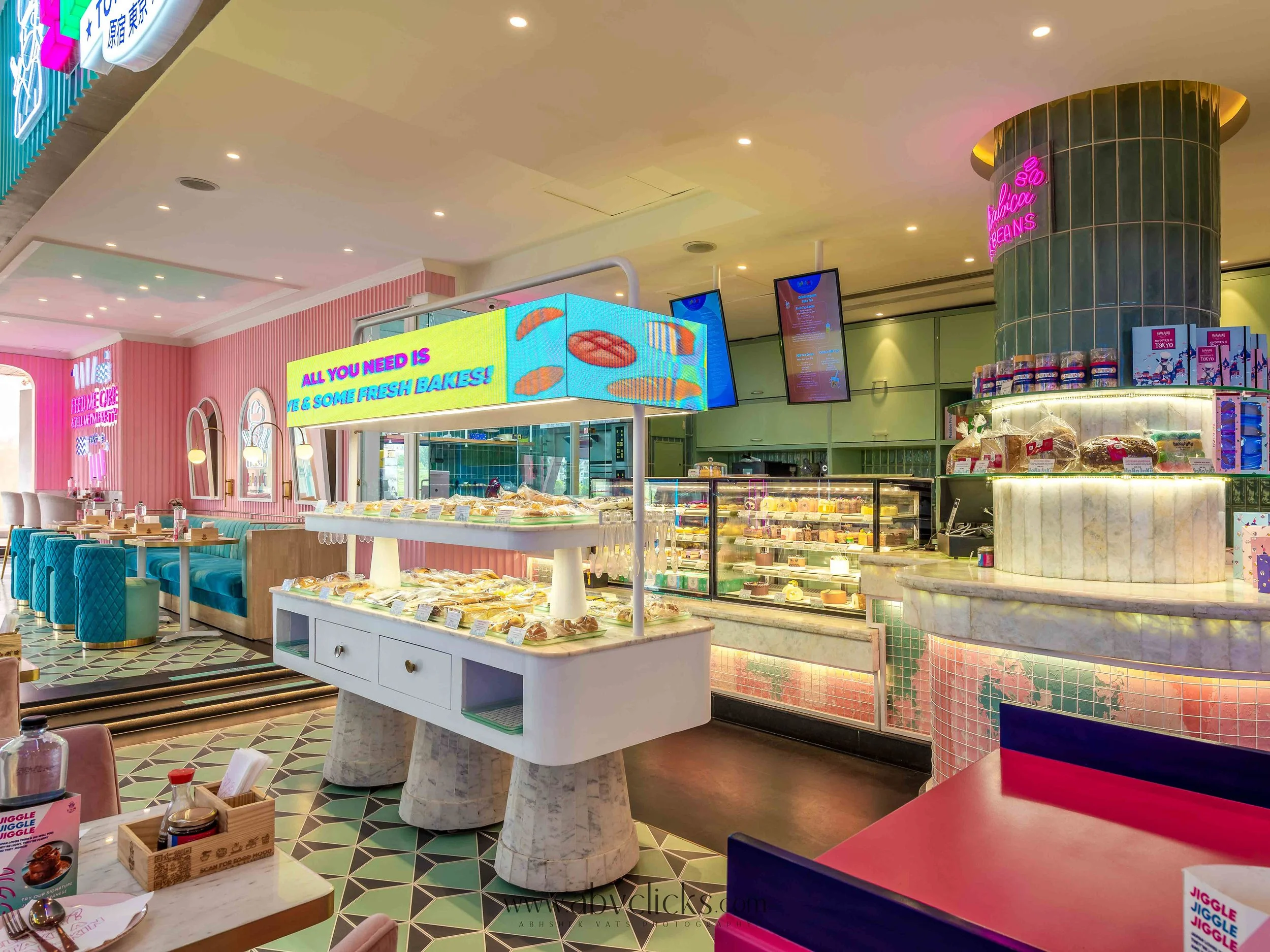 For brand Harajuku Tokyo Cafe, Interior of a bakery or cafe with pink and pastel decor, display cases filled with baked goods, and digital signs promoting baked items.