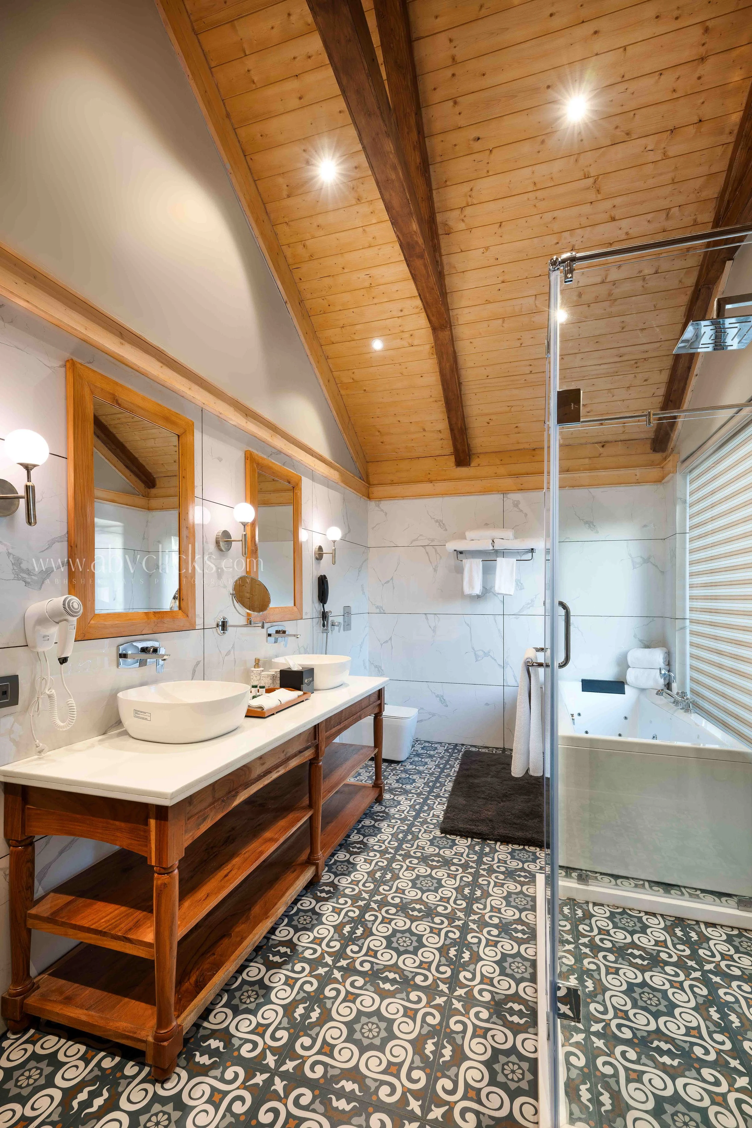 Bathroom with a wooden ceiling, large framed mirrors, double vessel sinks, patterned floor tiles, and a glass shower enclosure.