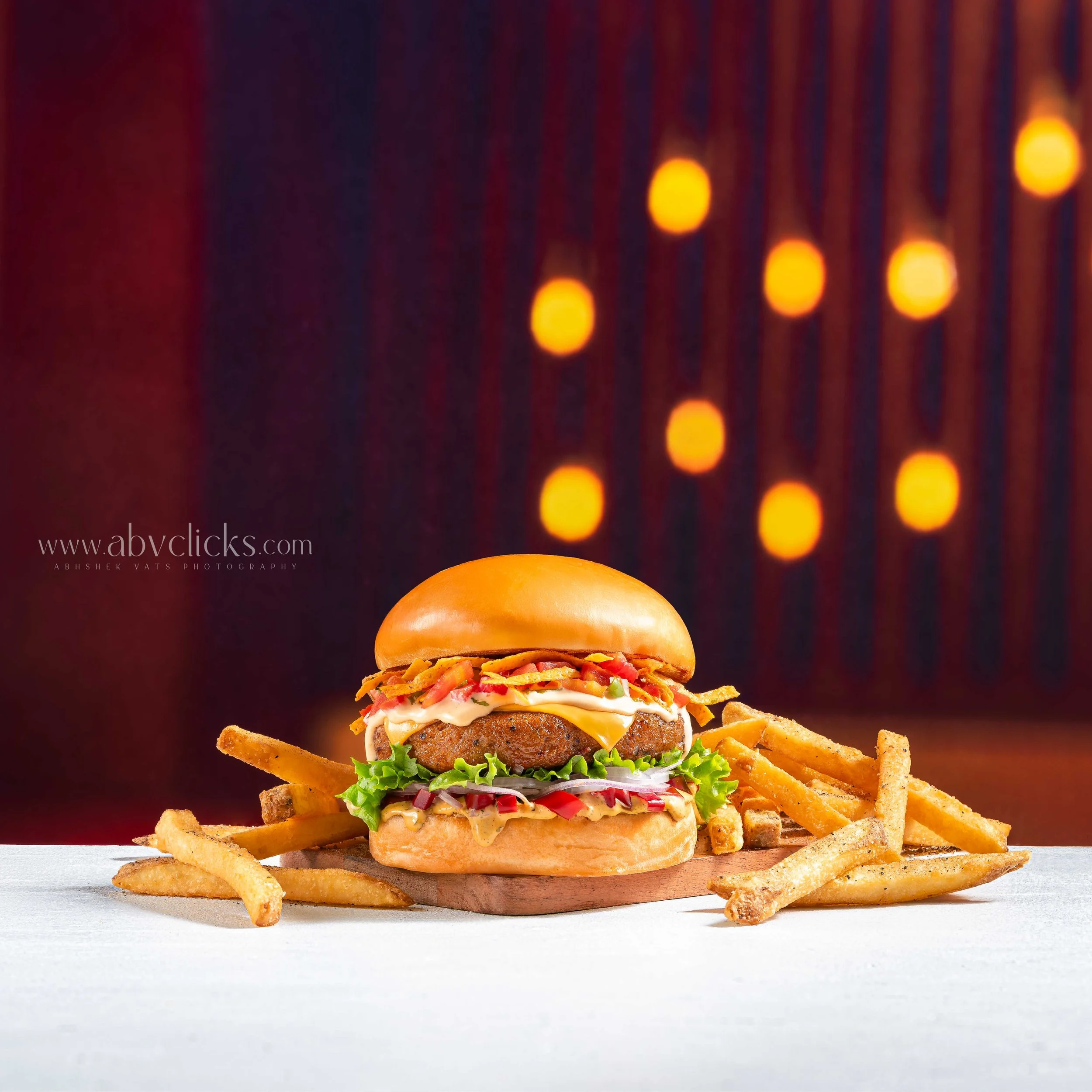 For Brand Chili's, A large burger with lettuce, tomato, cheese, and a meat patty, served with seasoned French fries, presented on a wooden board with a blurred background of warm-colored lights.