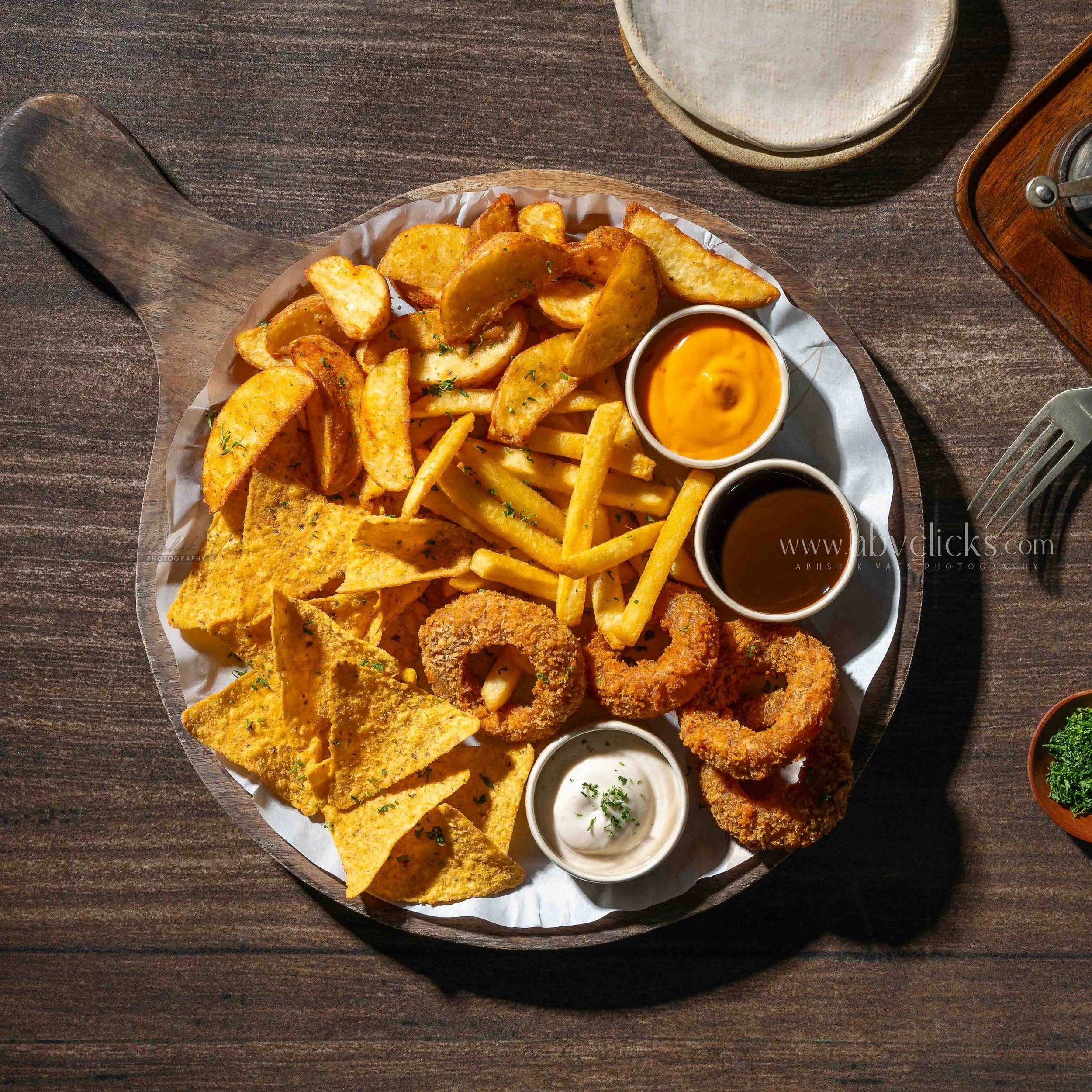 Plate of potato wedges, French fries, and fried fish served with dipping sauces on a wooden table.