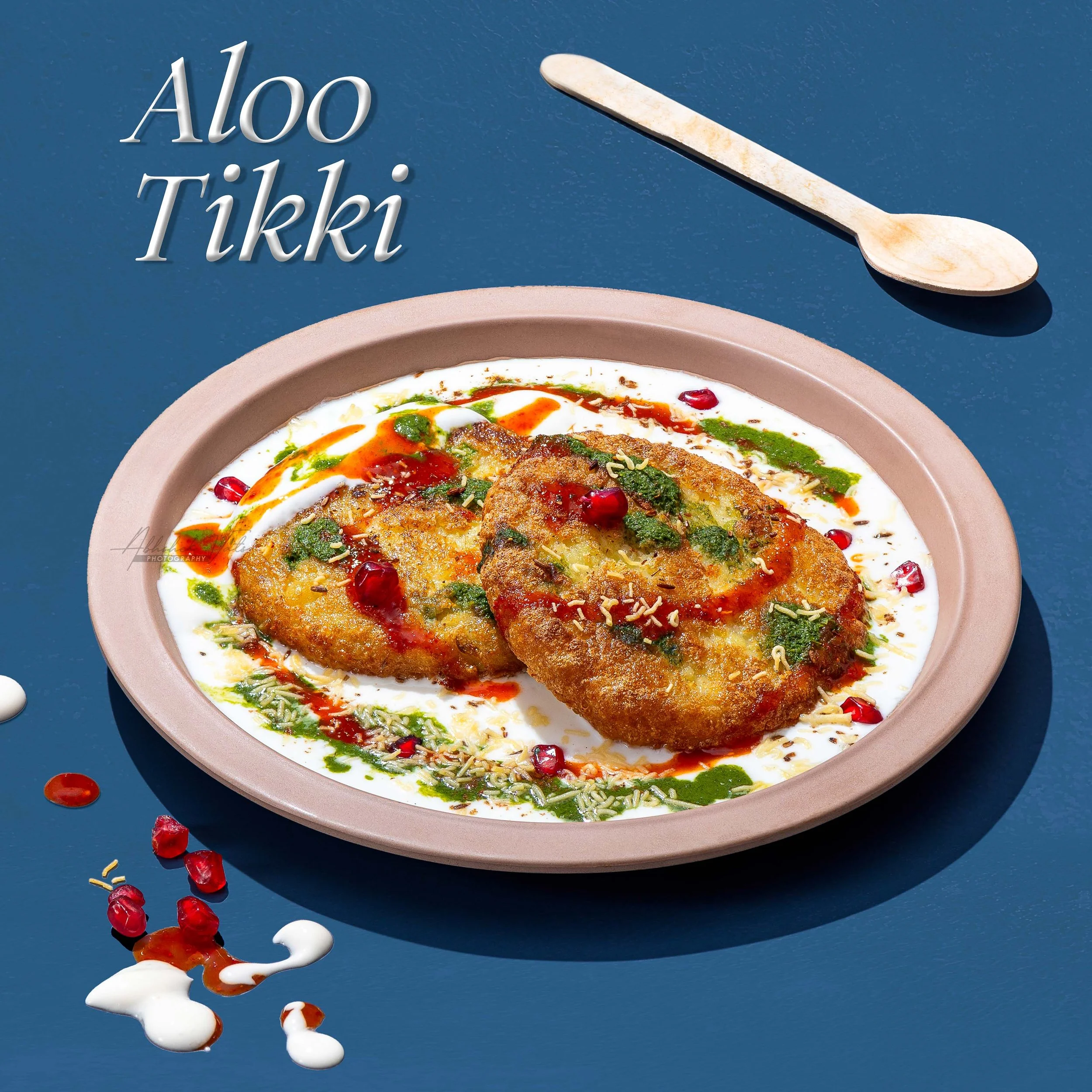 A bowl of Indian-style fish curry garnished with herbs and pomegranate seeds, with a wooden spoon on a blue background.
