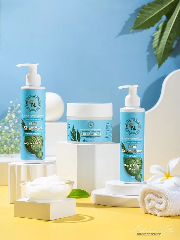 Collection of hair care products including shampoo, conditioner, and a spa mask on white platforms with towels, a bowl of cream, and a flower, set against a blue and yellow background.