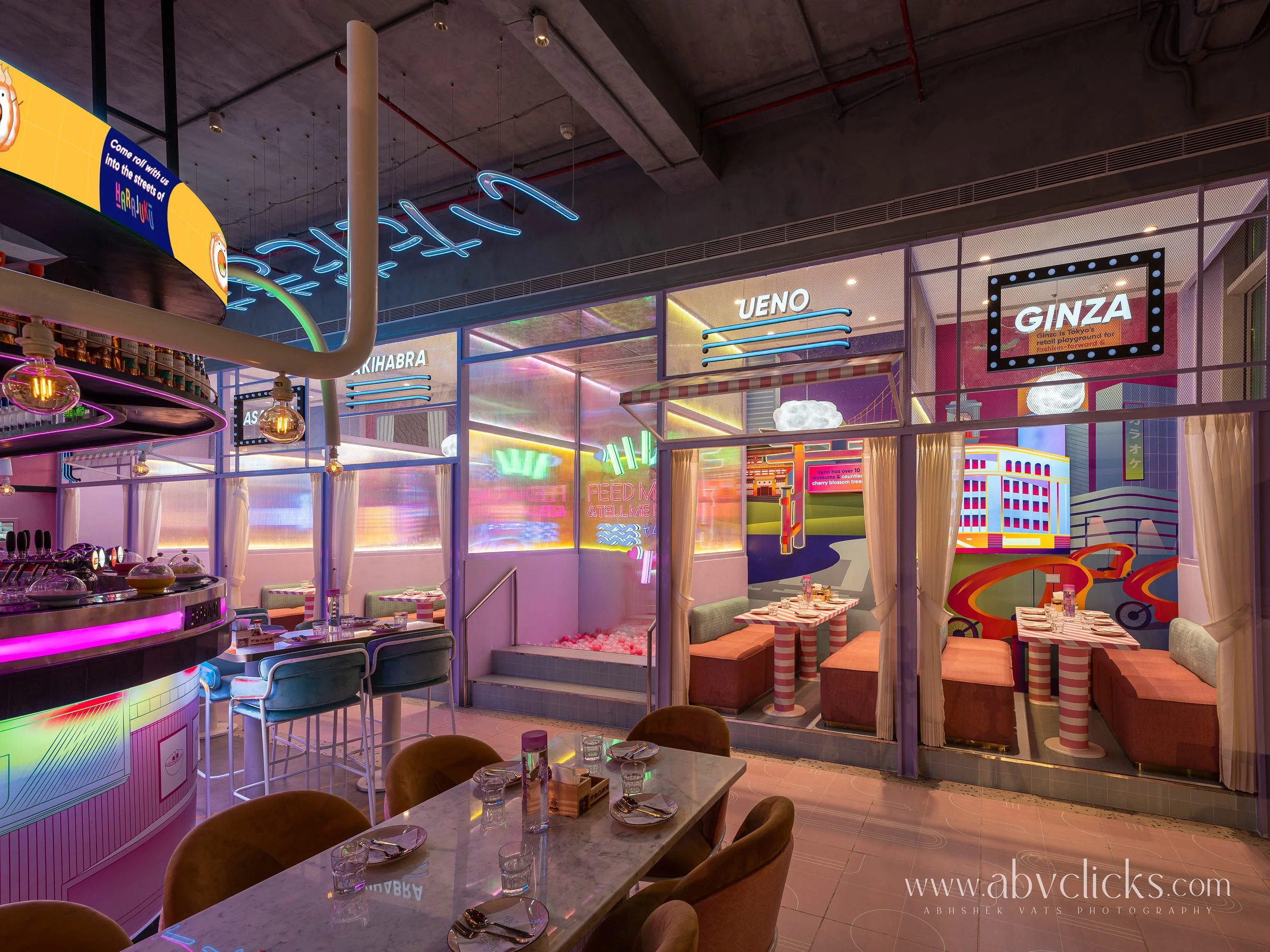 Interior of a colorful, neon-lit restaurant with tables, chairs, and digital signage for various districts in Tokyo, Japan including Harajuku, Shibuya, Ueno, and Ginza.