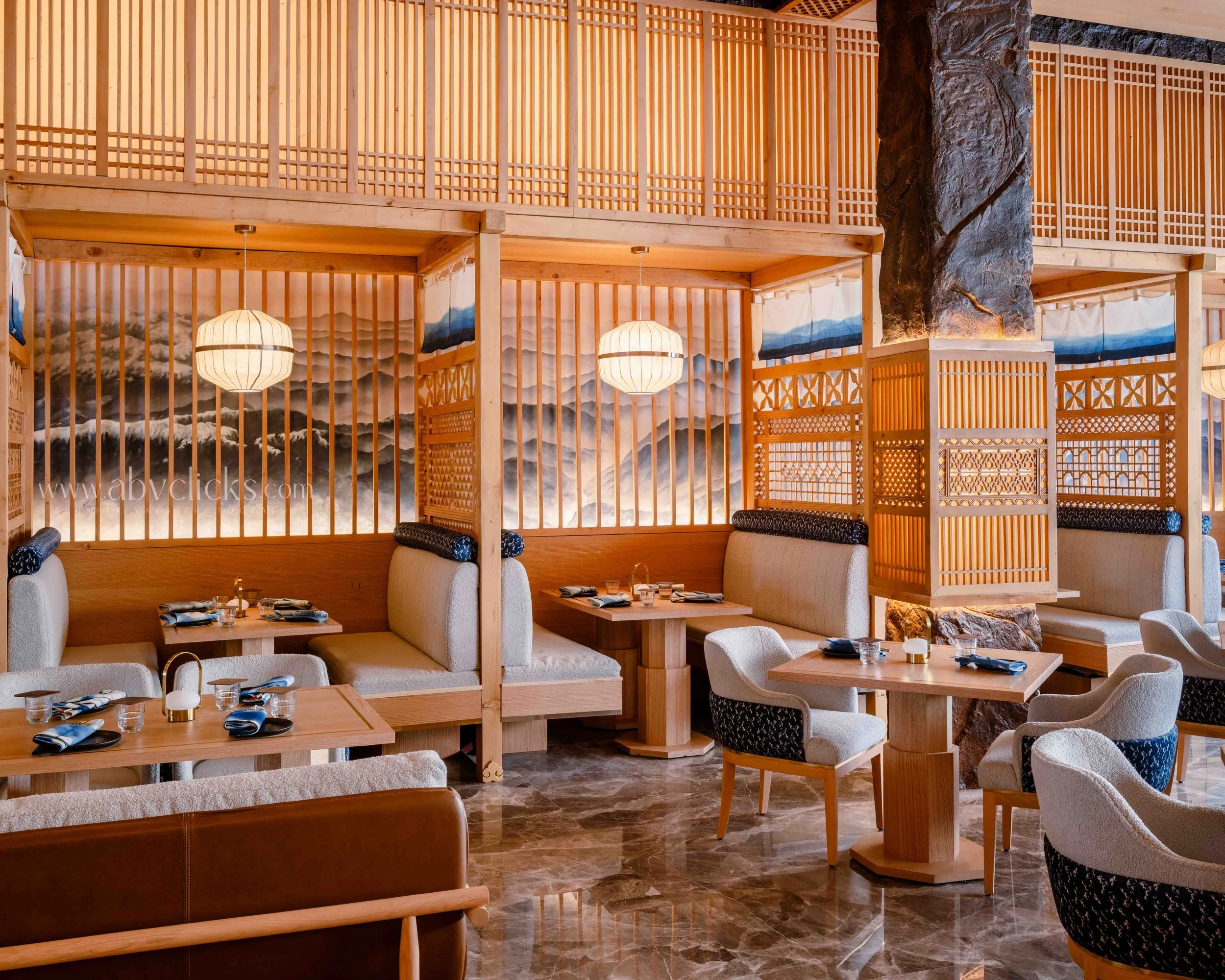Interior of a restaurant with wooden partitions, hanging lanterns, and traditional Japanese art murals on the walls, including mountains and clouds.