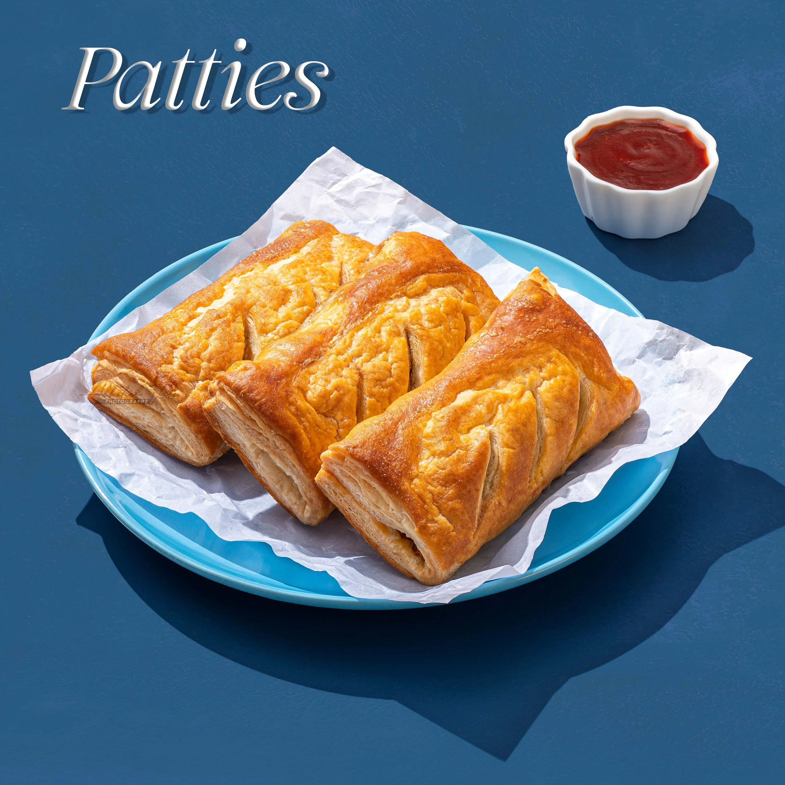Close-up of golden brown patties on white parchment paper in a blue bowl, with a small white ramekin of red sauce nearby on a blue surface.