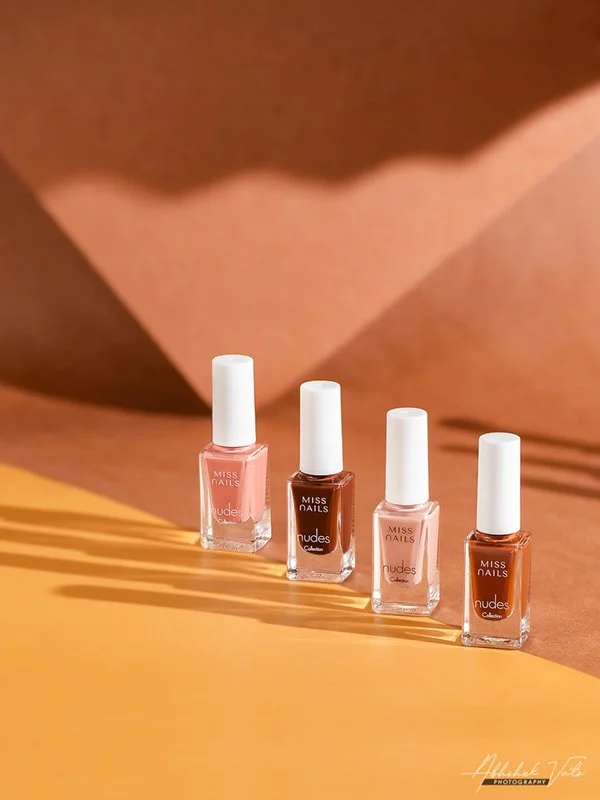 Four bottles of Miss Nails nail polish with white caps are arranged in a row on a two-tone background, casting shadows.