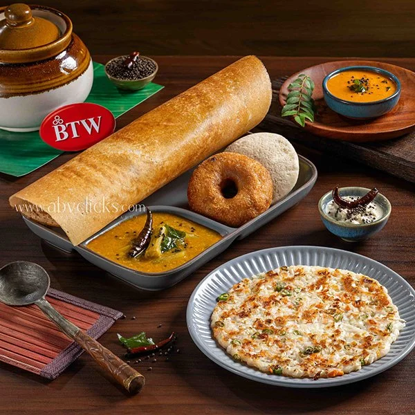 Indian meal with dosa, vada, idli, sambar, chutney, and curry on a table.