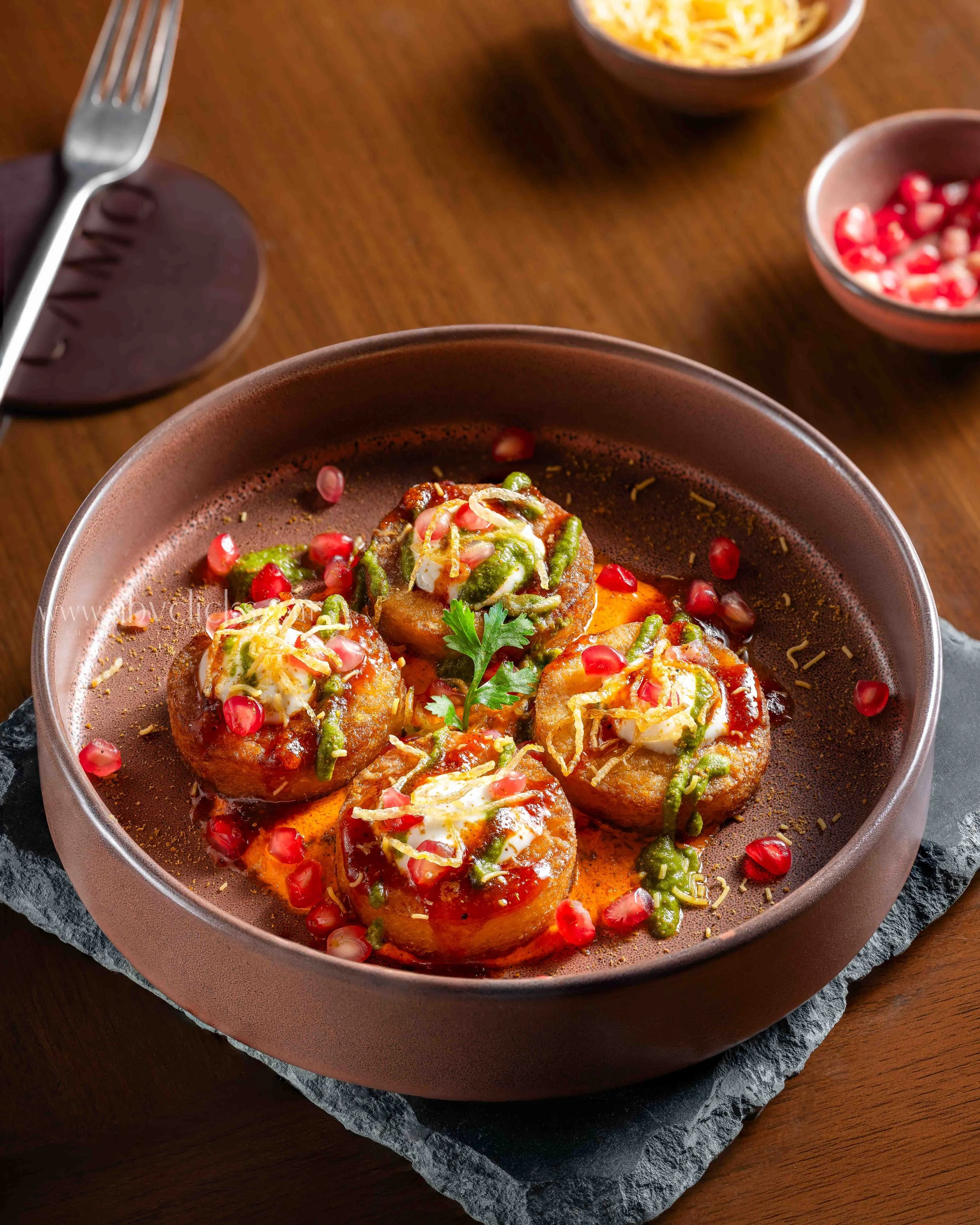 A bowl of food with four stuffed peppers topped with cheese, herbs, and pomegranate seeds on a dark slate serving platter.