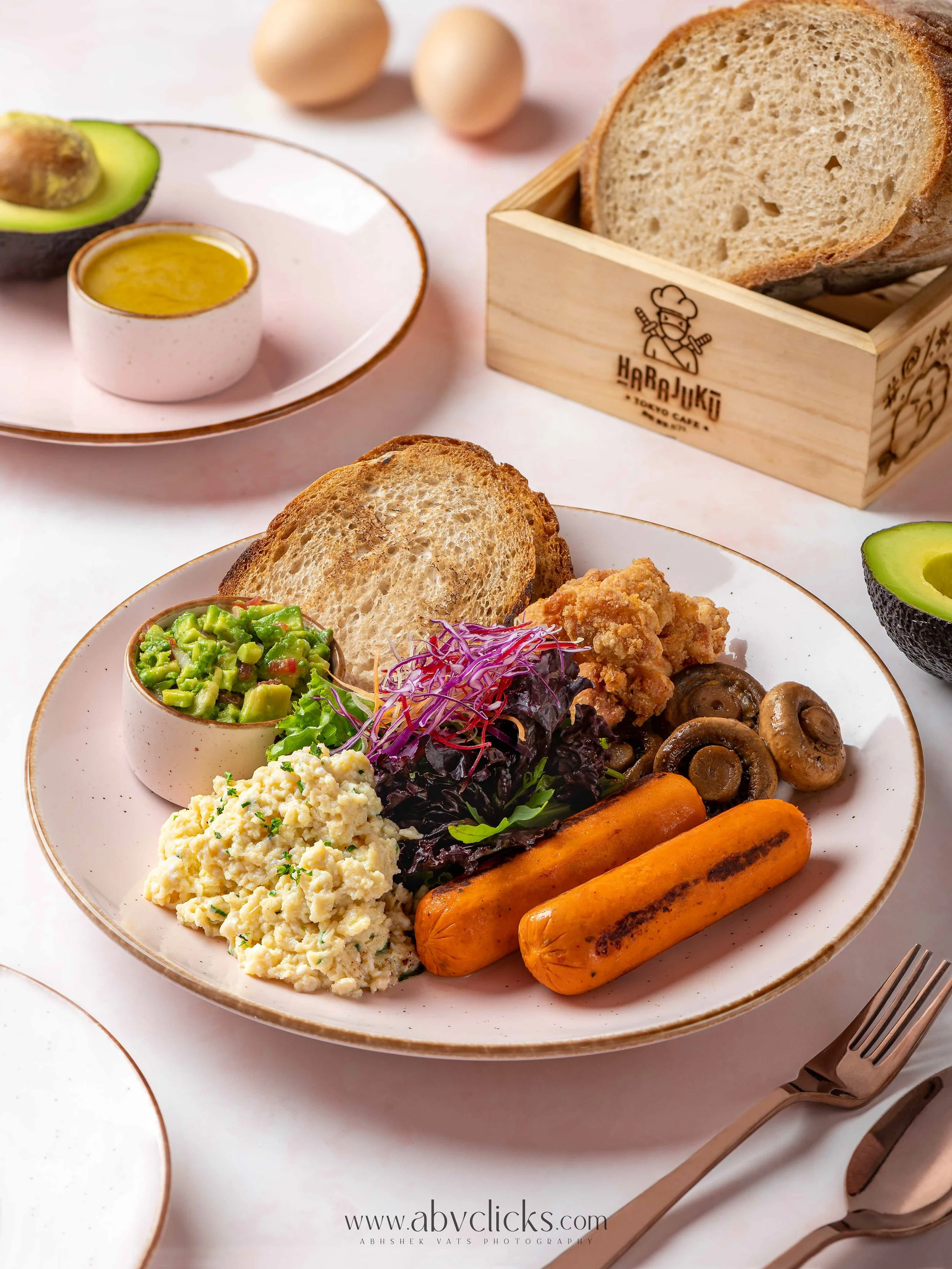 Plate of breakfast food including scrambled eggs, roasted carrots, sautéed mushrooms, salad with purple cabbage, and slices of toasted bread, with a side of avocado and an egg in the background.