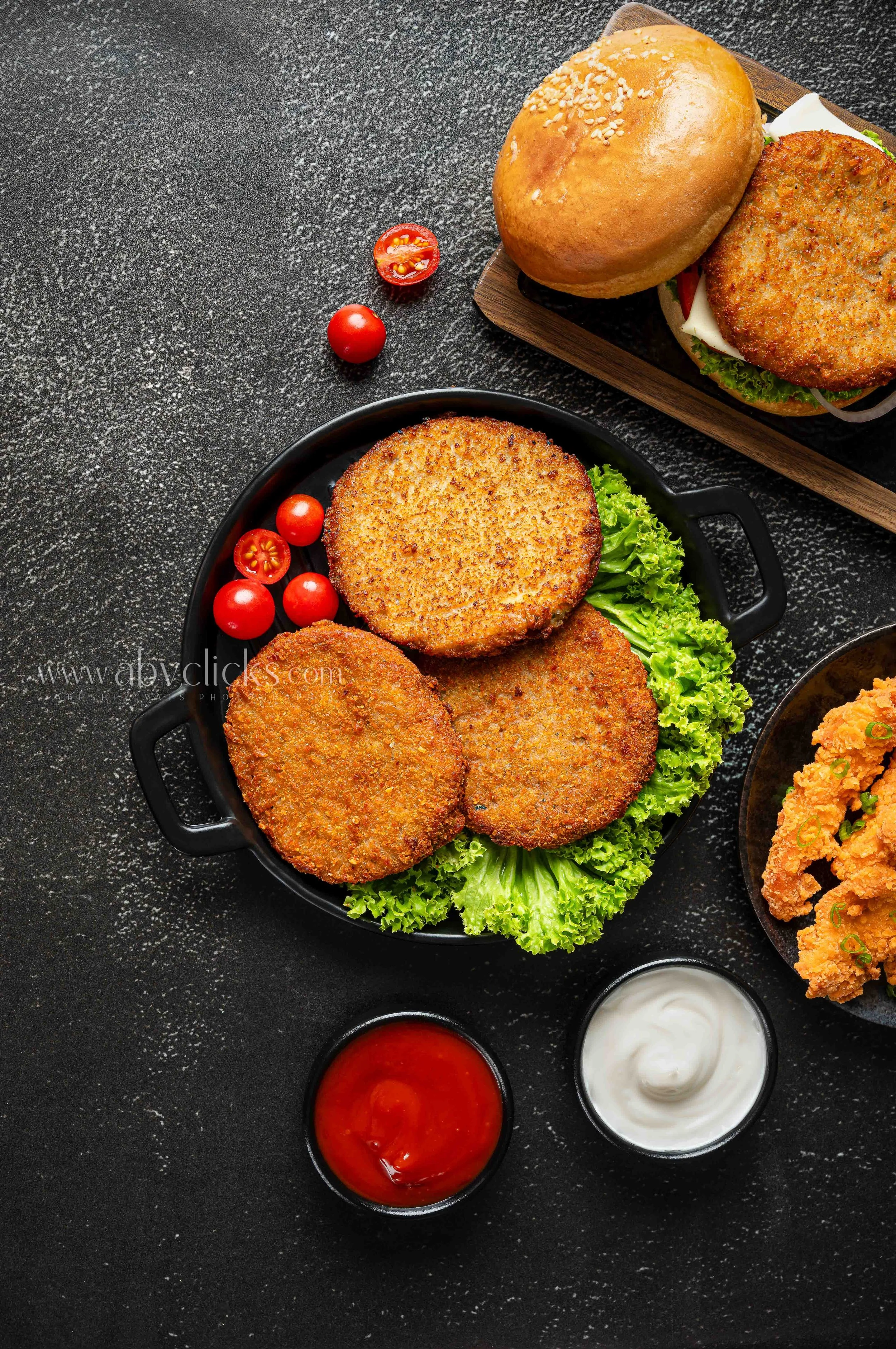 Fried crab cakes served with lettuce, cherry tomatoes, and various dipping sauces on a black textured surface.