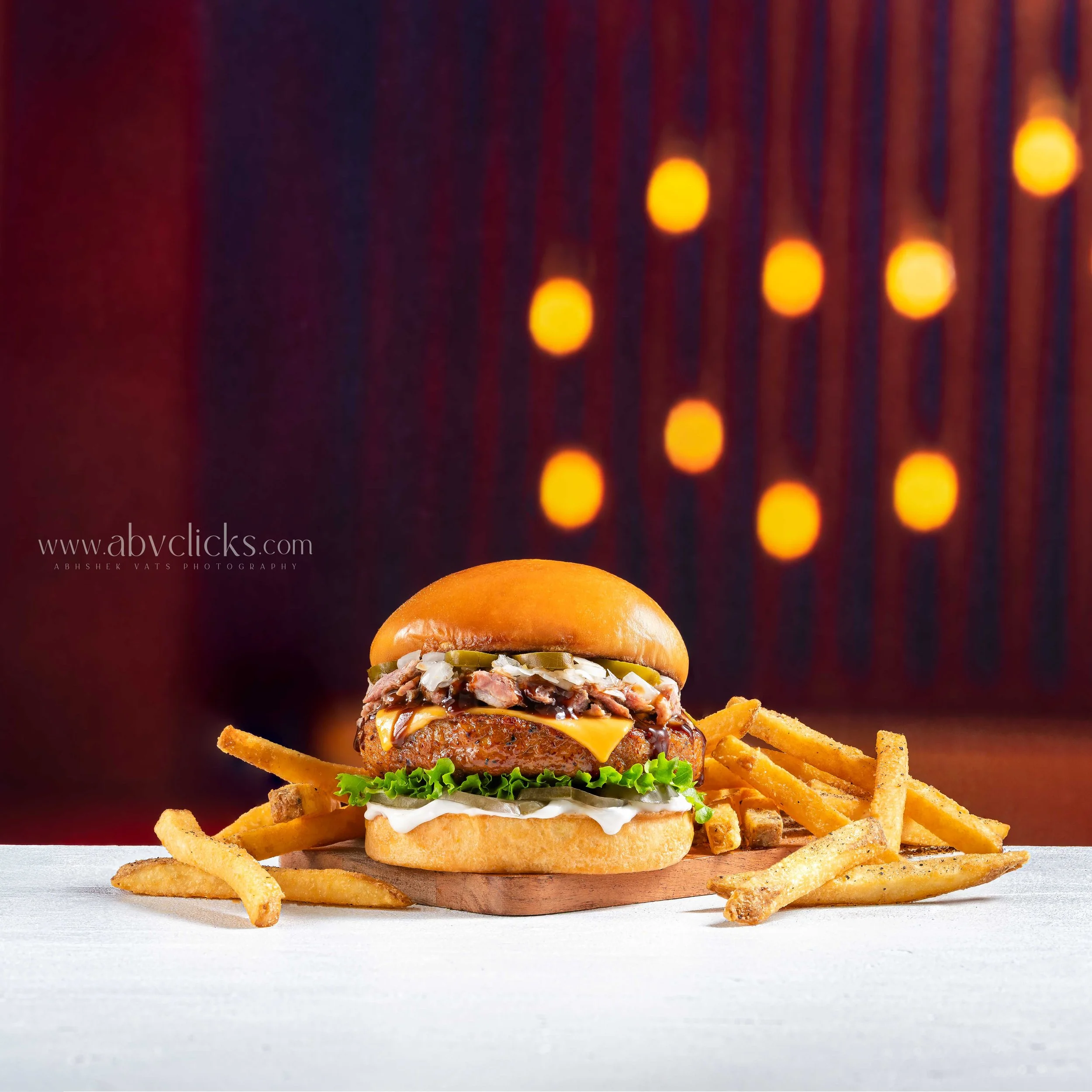A gourmet hamburger with a beef patty, melted cheese, mayonnaise, onions, and lettuce in a bun, served with French fries on a white surface.