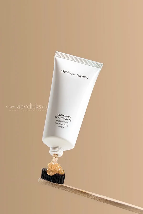 Toothpaste tube labeled 'Smilez Spec Whitening Toothpaste Peppermint Fluoride Free 50g' is squeezing a dab onto a toothbrush over a plain beige background.