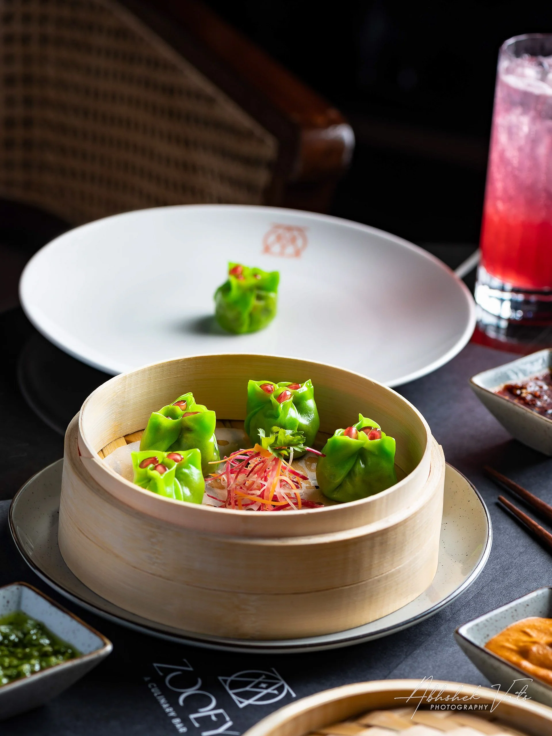 Steamed green dumplings with red filling in bamboo steamer, served with shredded vegetables.