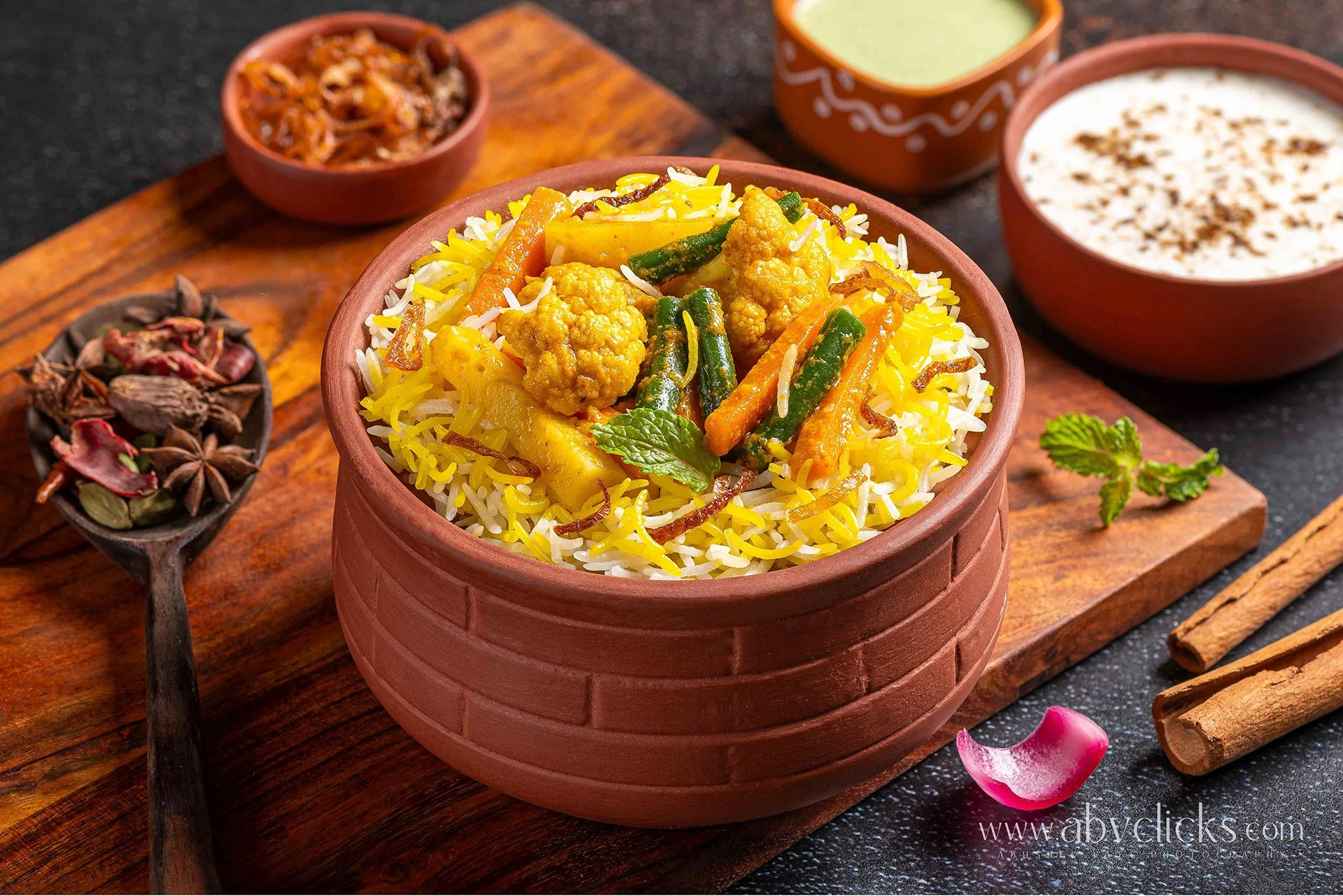 A bowl of Indian vegetable pulao rice with cauliflower, carrots, and green beans, garnished with cilantro, on a wooden serving tray surrounded by spices and sauces.