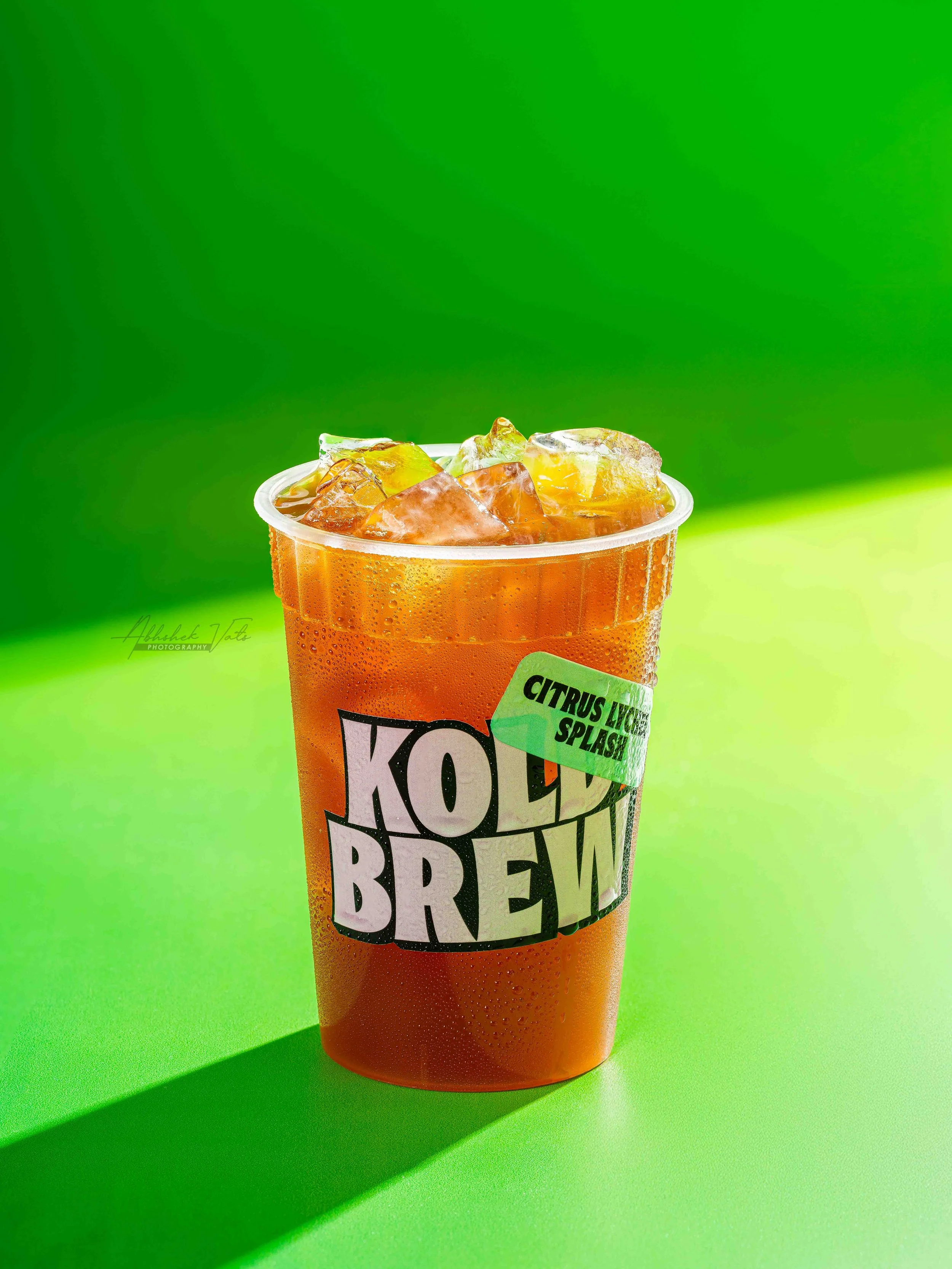 A cold orange beverage in a translucent plastic cup with ice cubes, against a vibrant green background.