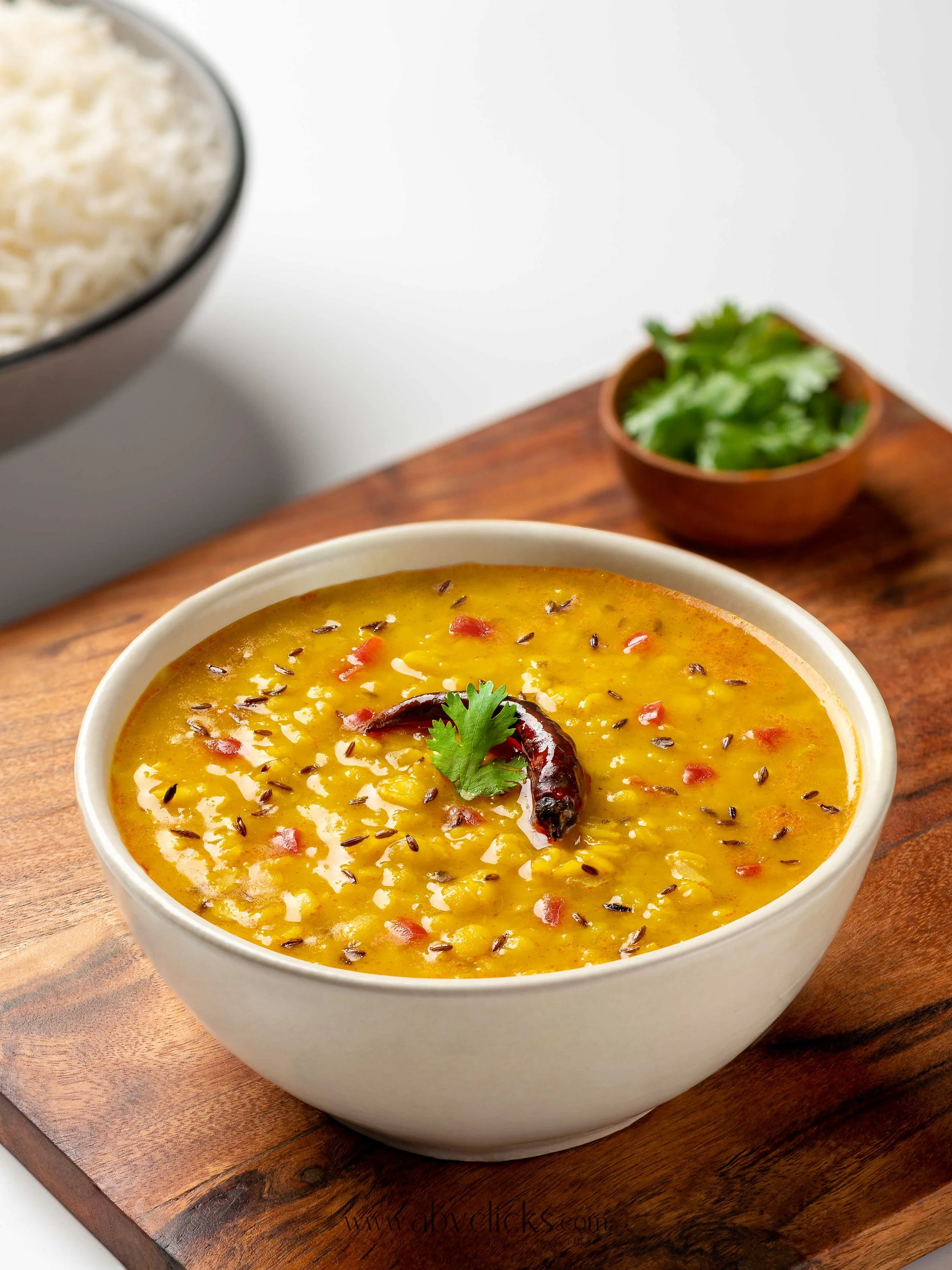 A bowl of yellow lentil soup garnished with red chili, cilantro, and spices, placed on a wooden serving board.