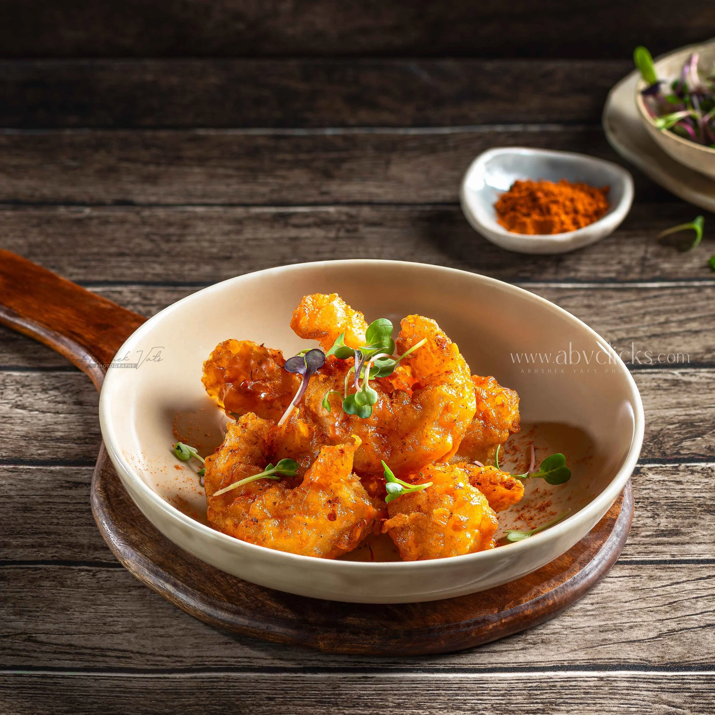 Close-up of a bowl of crispy fried cauliflower florets garnished with microgreens, placed on a dark wooden surface.