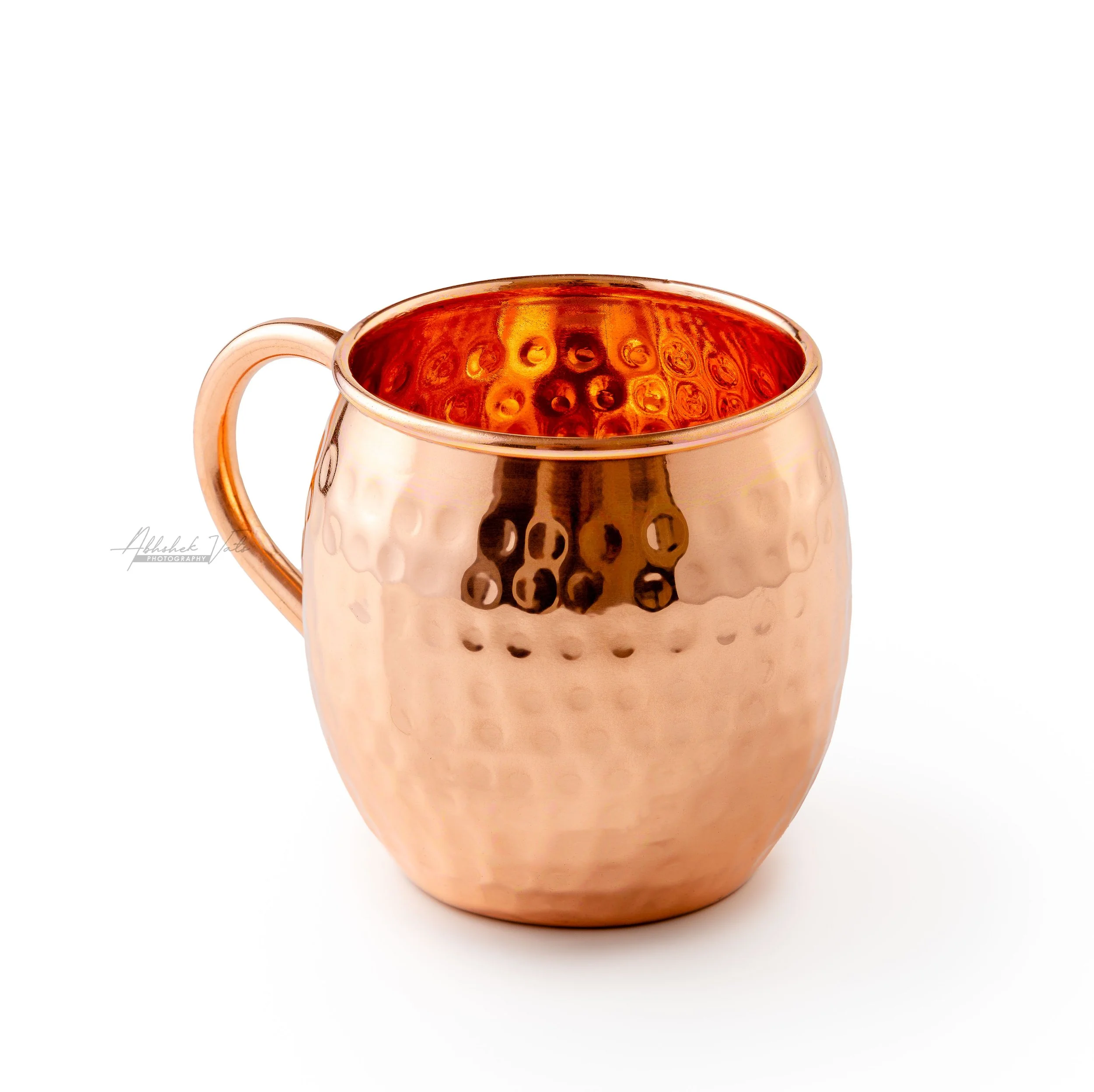 A copper mug filled with a beverage, white interior, textured exterior, and a handle on the left side, set against a white background.