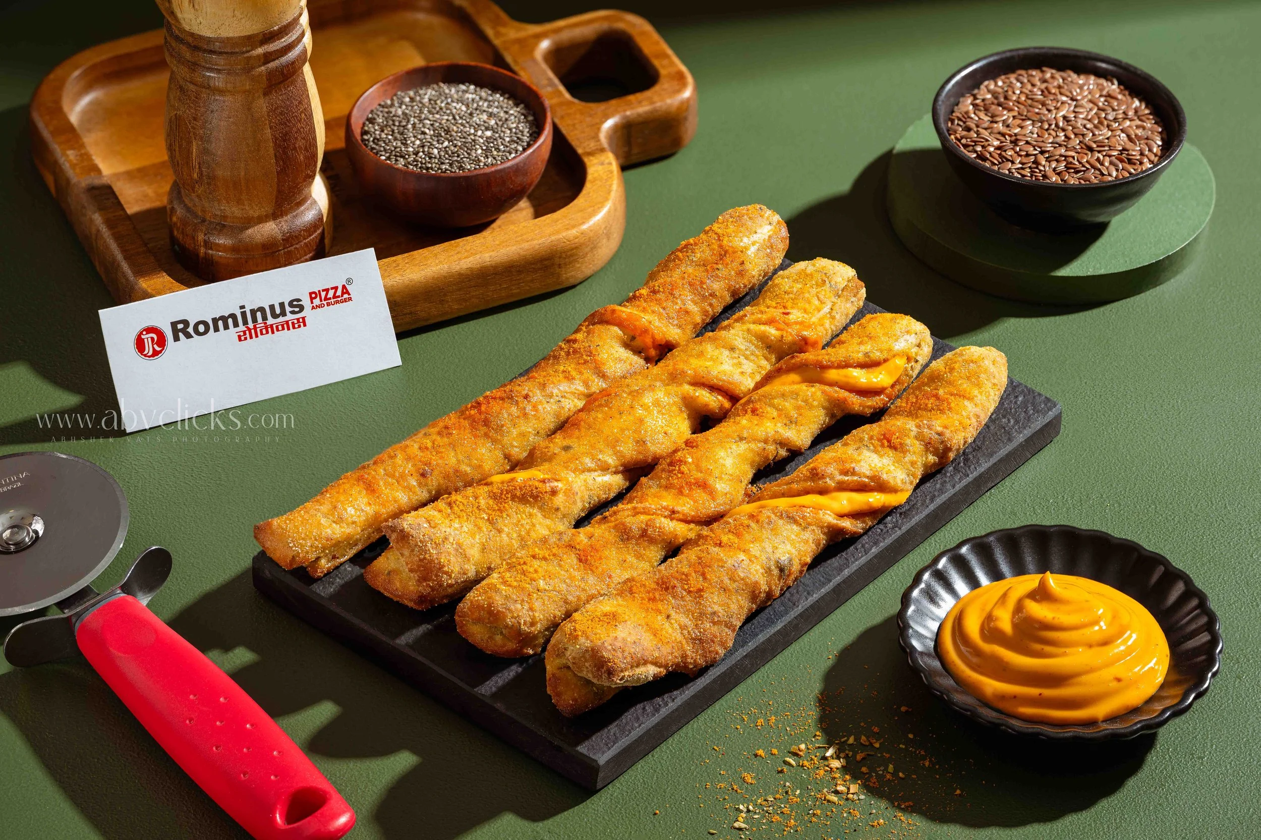 Close-up of fried fish fillets with a crispy golden coating, placed on a black slate tray, accompanied by a small bowl of yellow sauce, with a green table surface in the background.