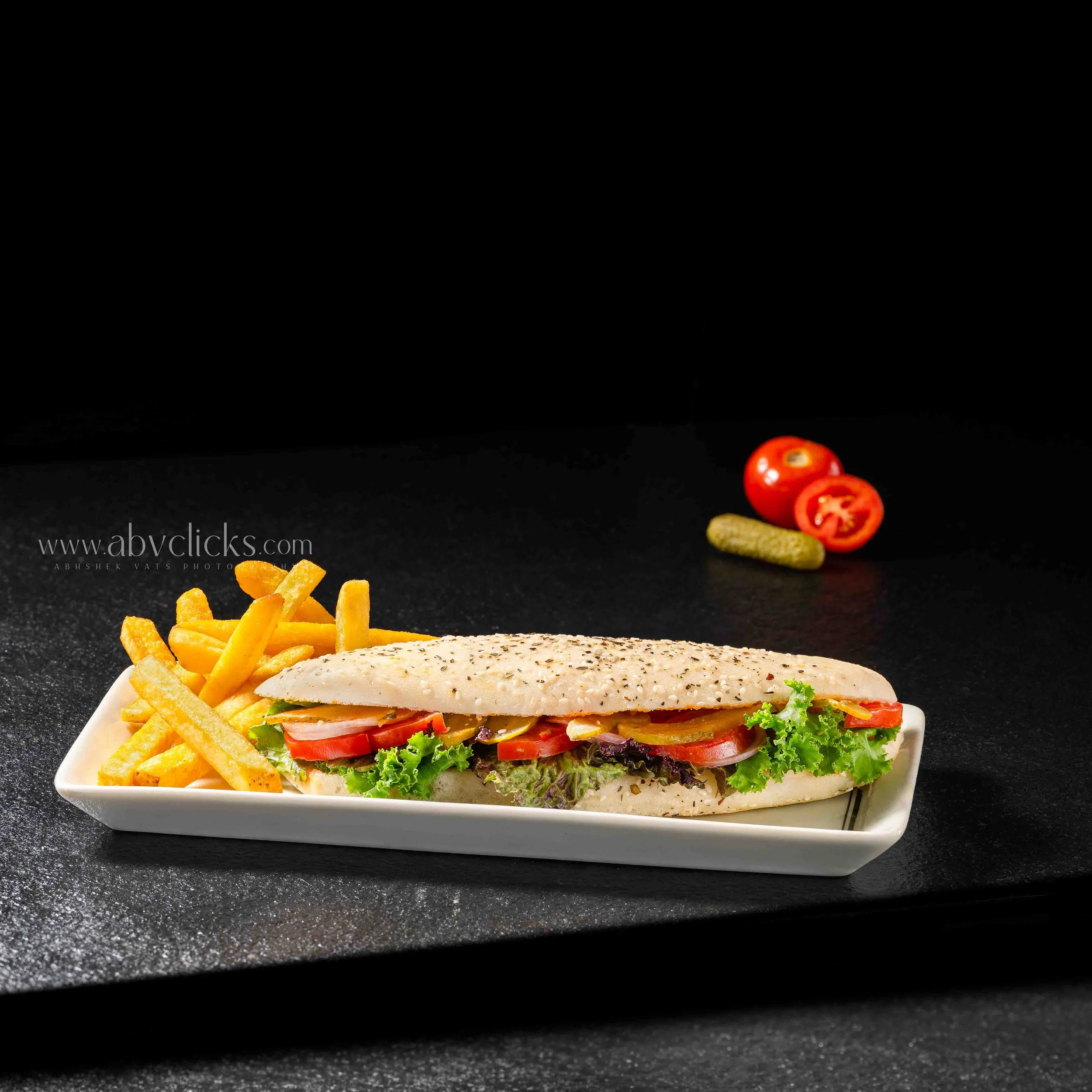 A sandwich on a white plate with French fries and sliced tomatoes. The sandwich has lettuce, tomato slices, and a seasoned chicken fillet in a bun.