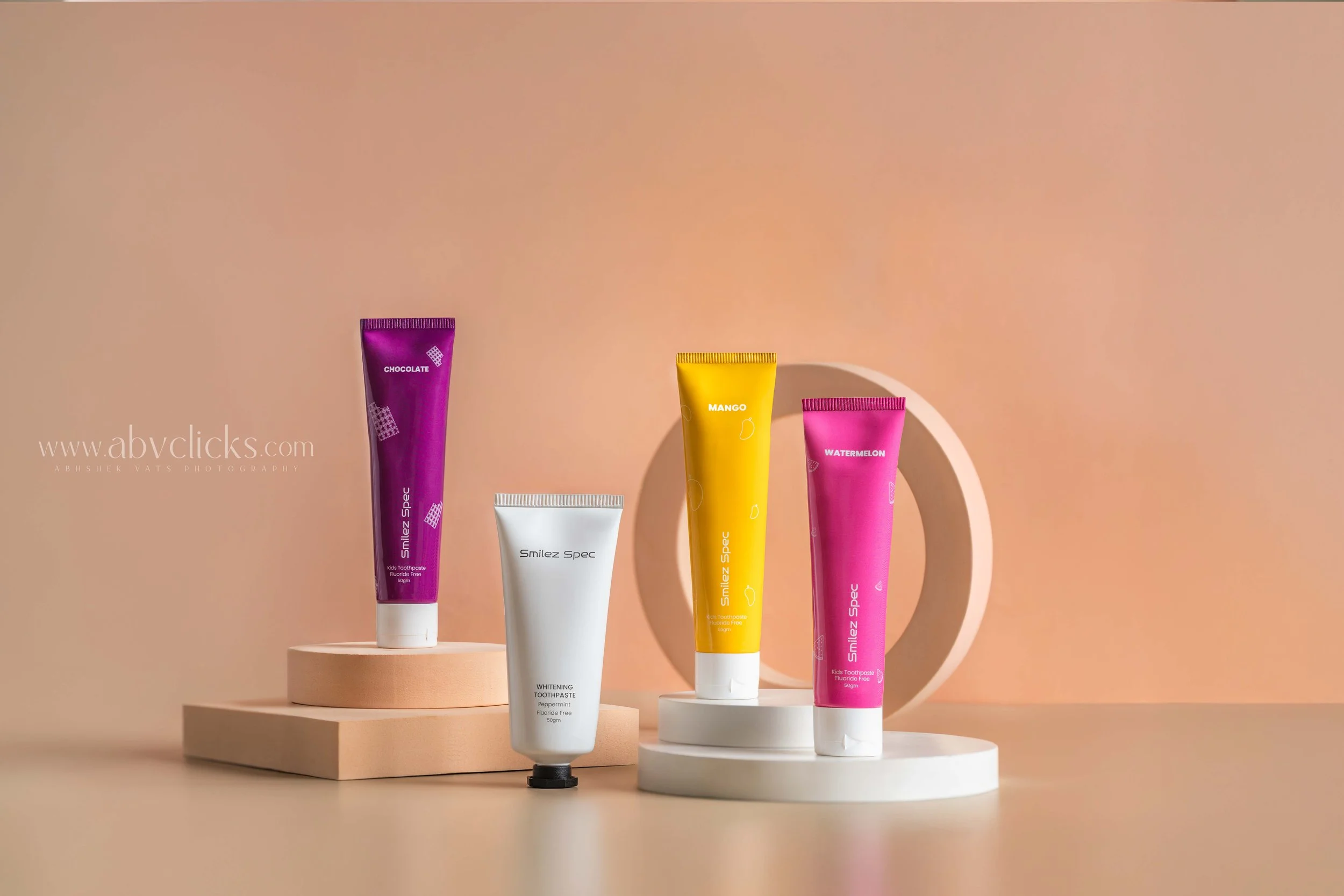 Colorful tubes of toothpaste arranged on circular platforms with a peach-pink background and neutral-colored props.